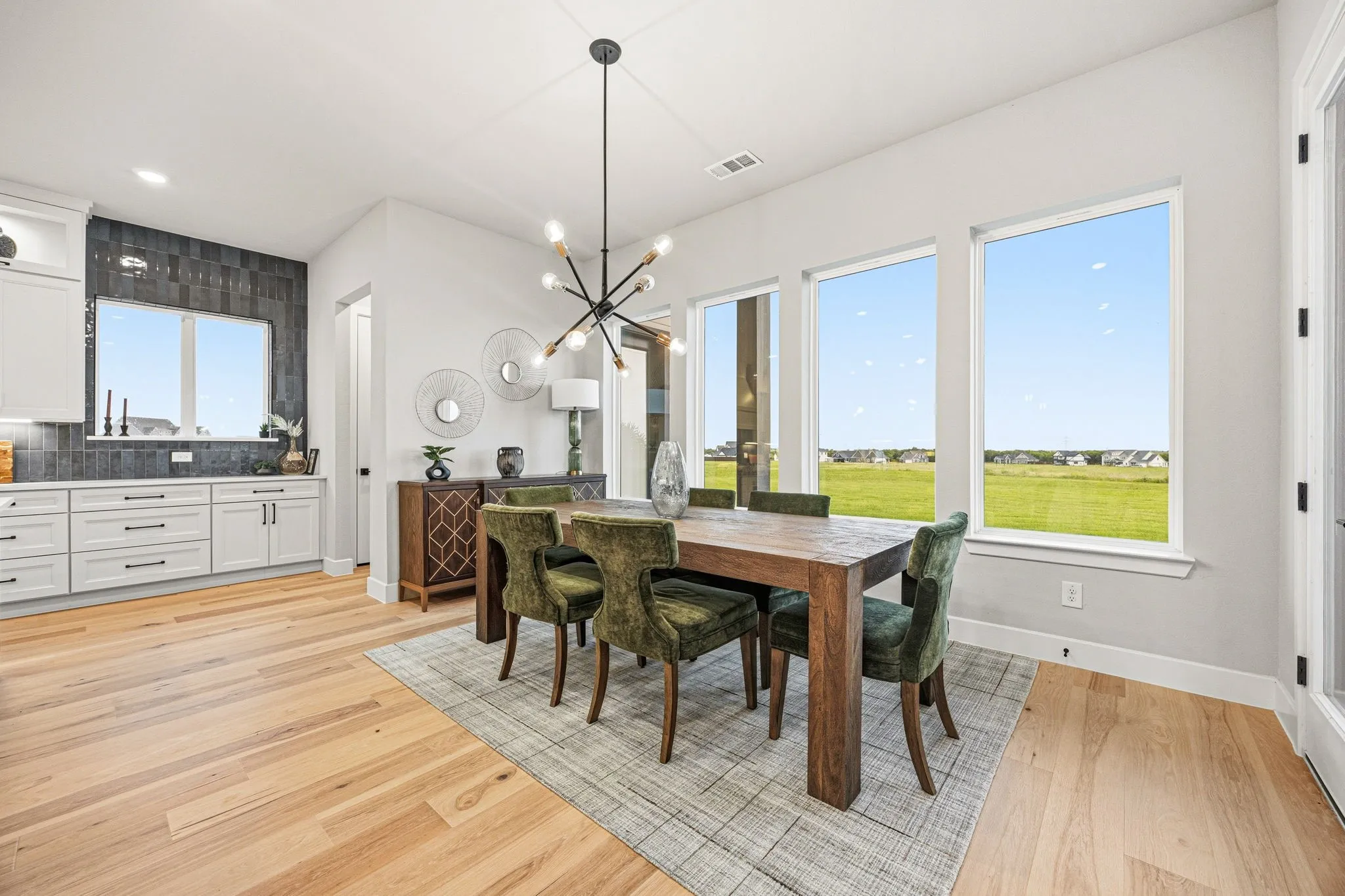 Open-concept living space featuring wood-finish flooring, a contemporary chandelier, multiple large windows, white cabinetry, and a dark tile backsplash