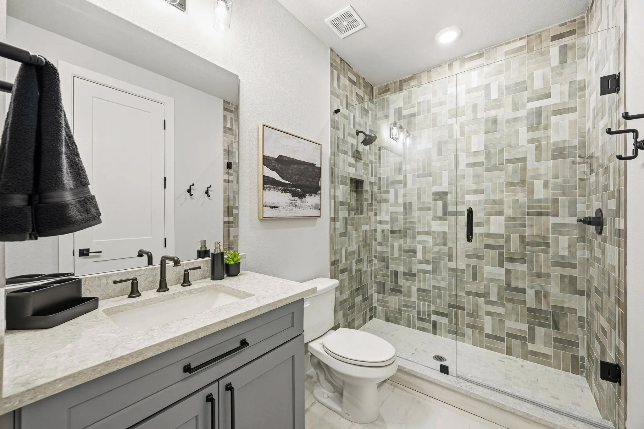 Contemporary bathroom featuring a glass-enclosed shower with geometric tile work, a vanity with a light-toned countertop, and dark-finish fixtures