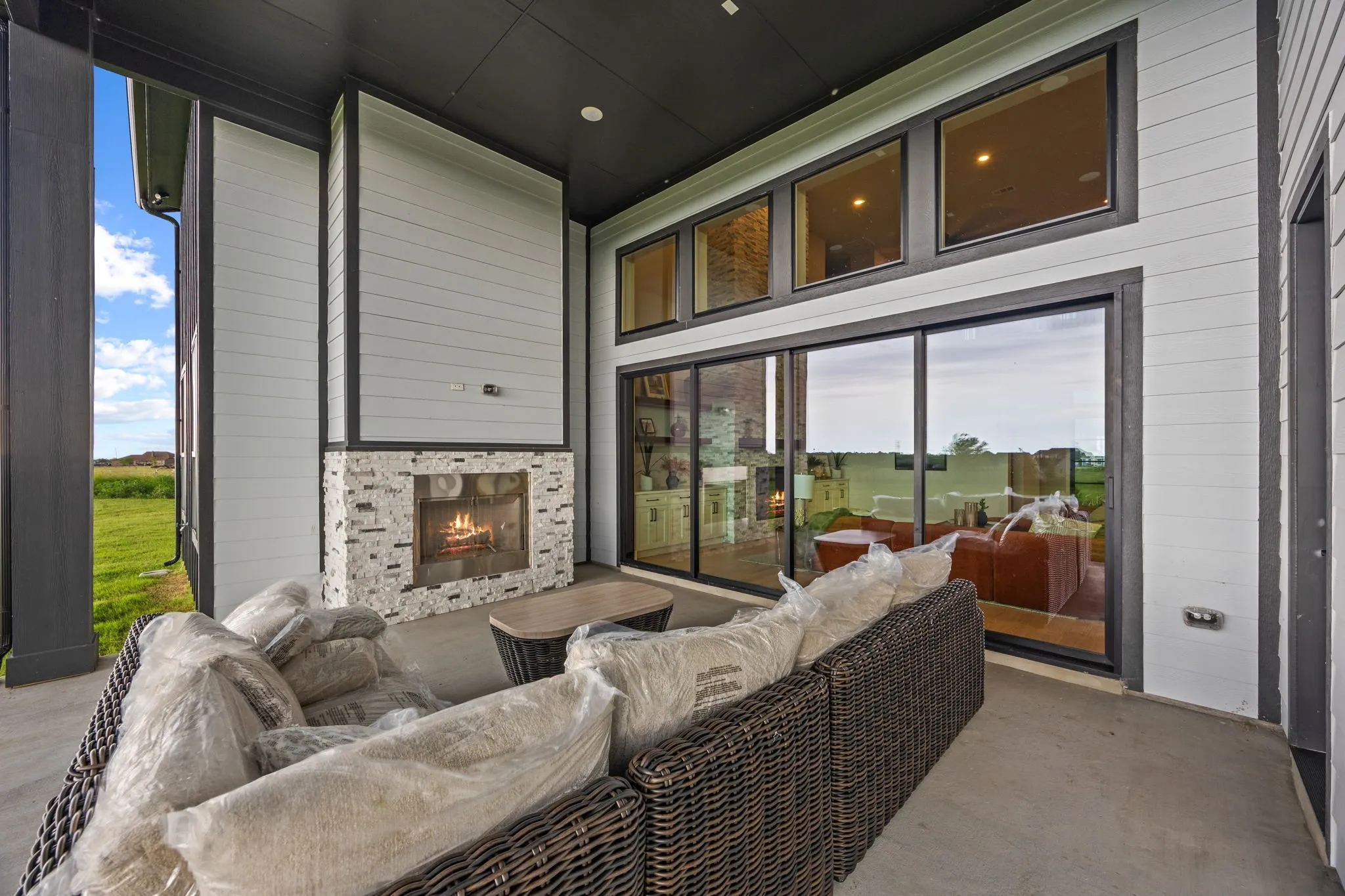 Covered outdoor patio featuring a stone fireplace, large sliding glass doors, three upper transom windows, concrete flooring, and horizontal siding
