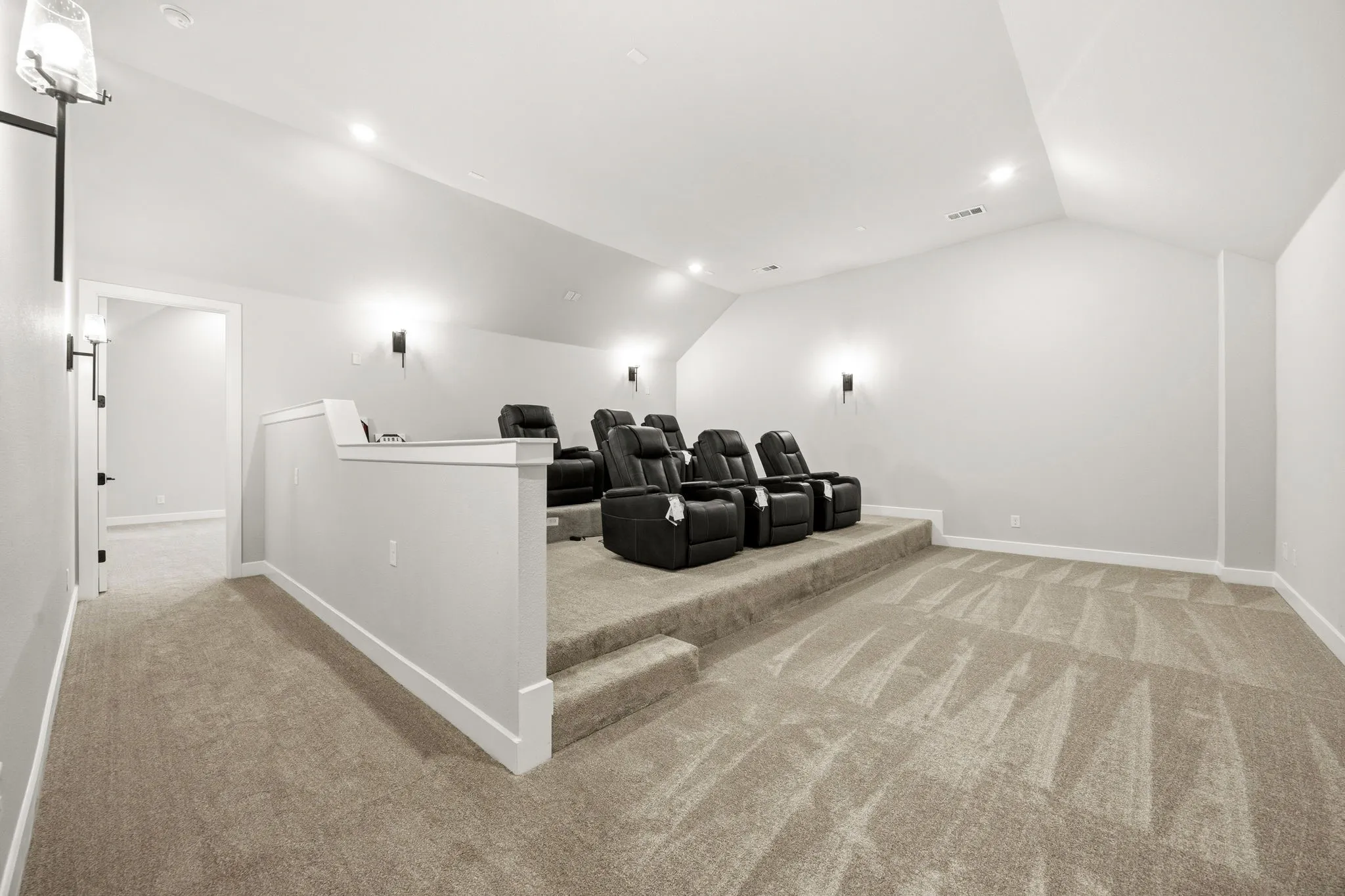 Dedicated media room featuring tiered seating, recessed ceiling lighting, wall sconces, and neutral-toned carpeting