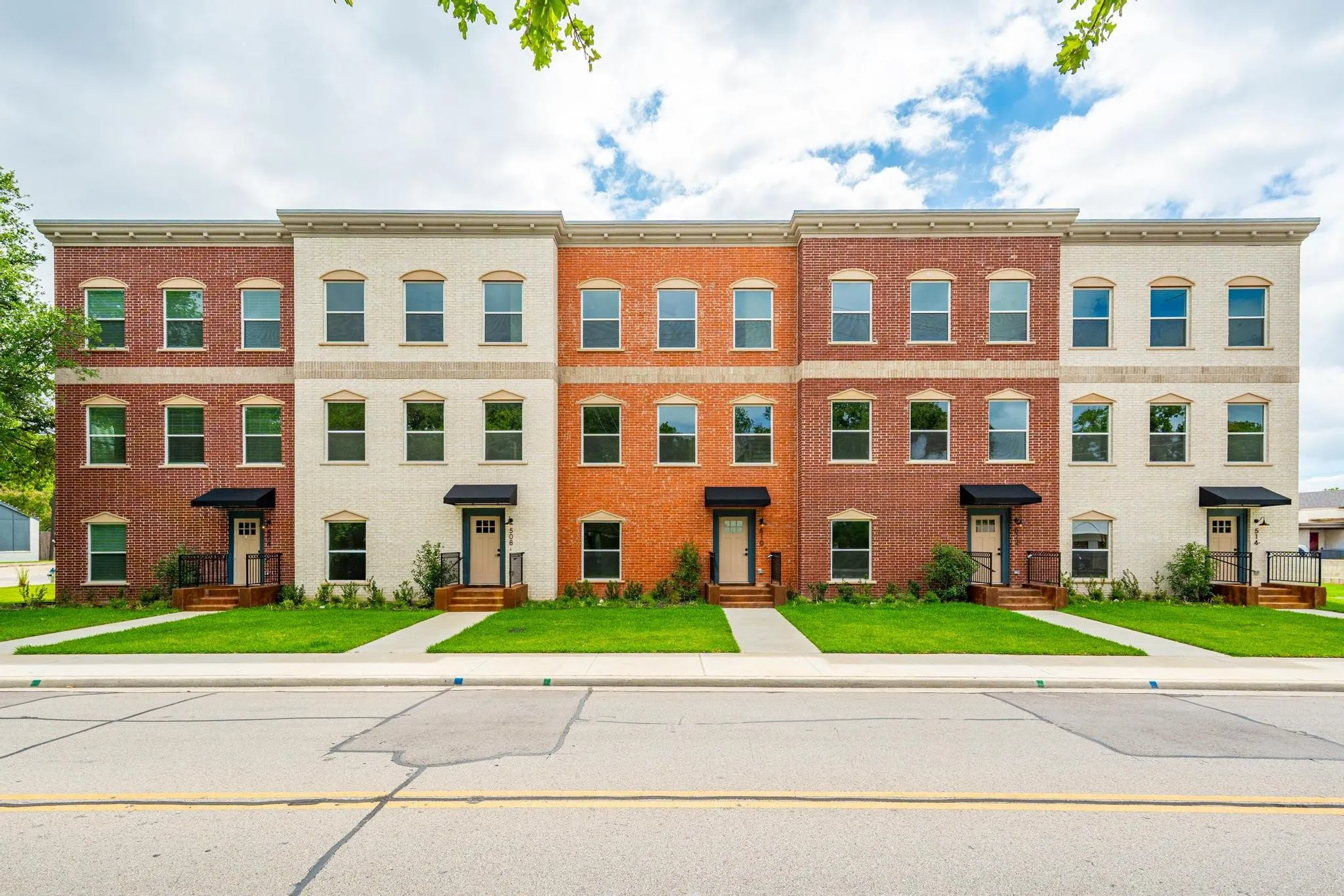 Multi-story townhome exterior featuring a brick facade with alternating red and cream hues