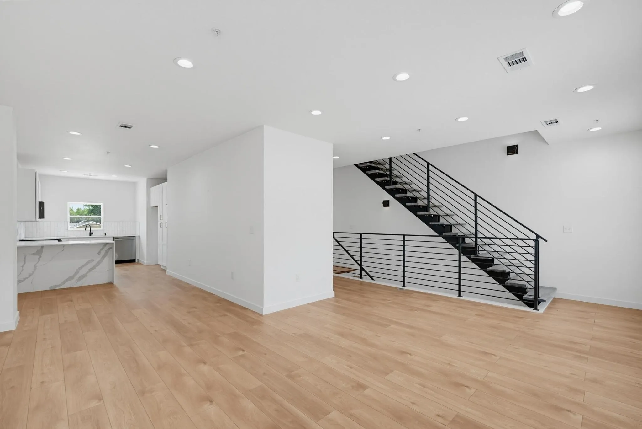 Open-concept living space featuring light wood-finish flooring, recessed lighting, and a contemporary staircase with black metal railings