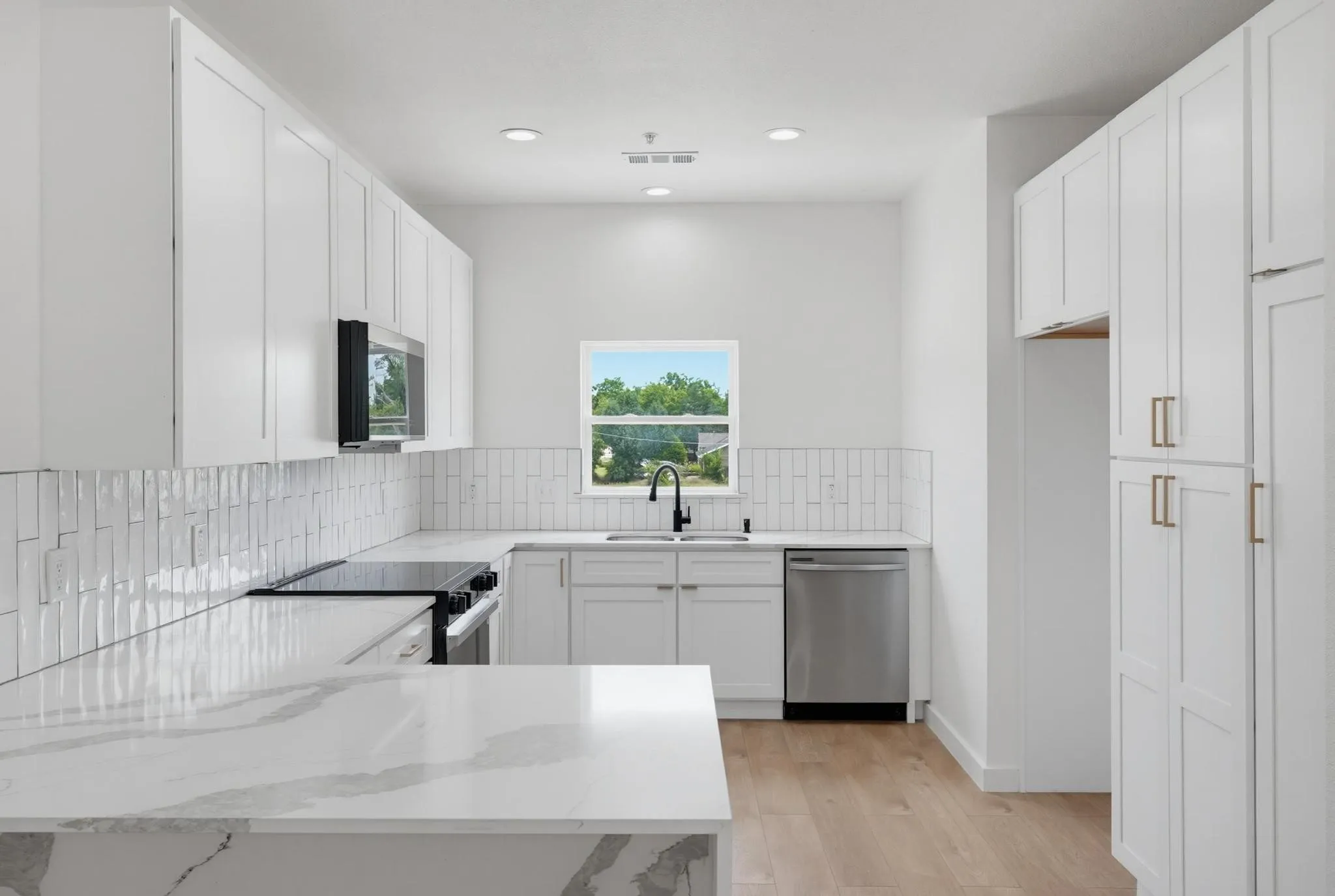 Modern kitchen featuring white shaker cabinetry, stainless steel appliances, and wood-finish flooring