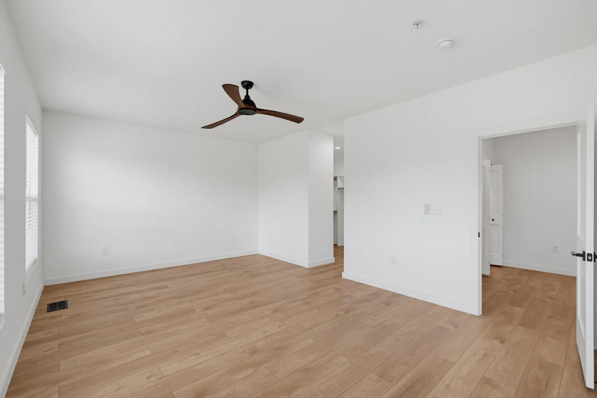 Spacious room featuring wood-finish flooring, crisp white walls, and a contemporary ceiling fan
