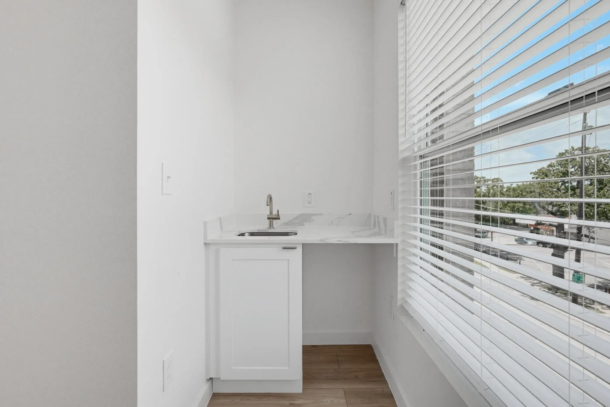 Single-basin sink with a gooseneck faucet, set within a white countertop and featuring a built-in cabinet with a shaker-style door
