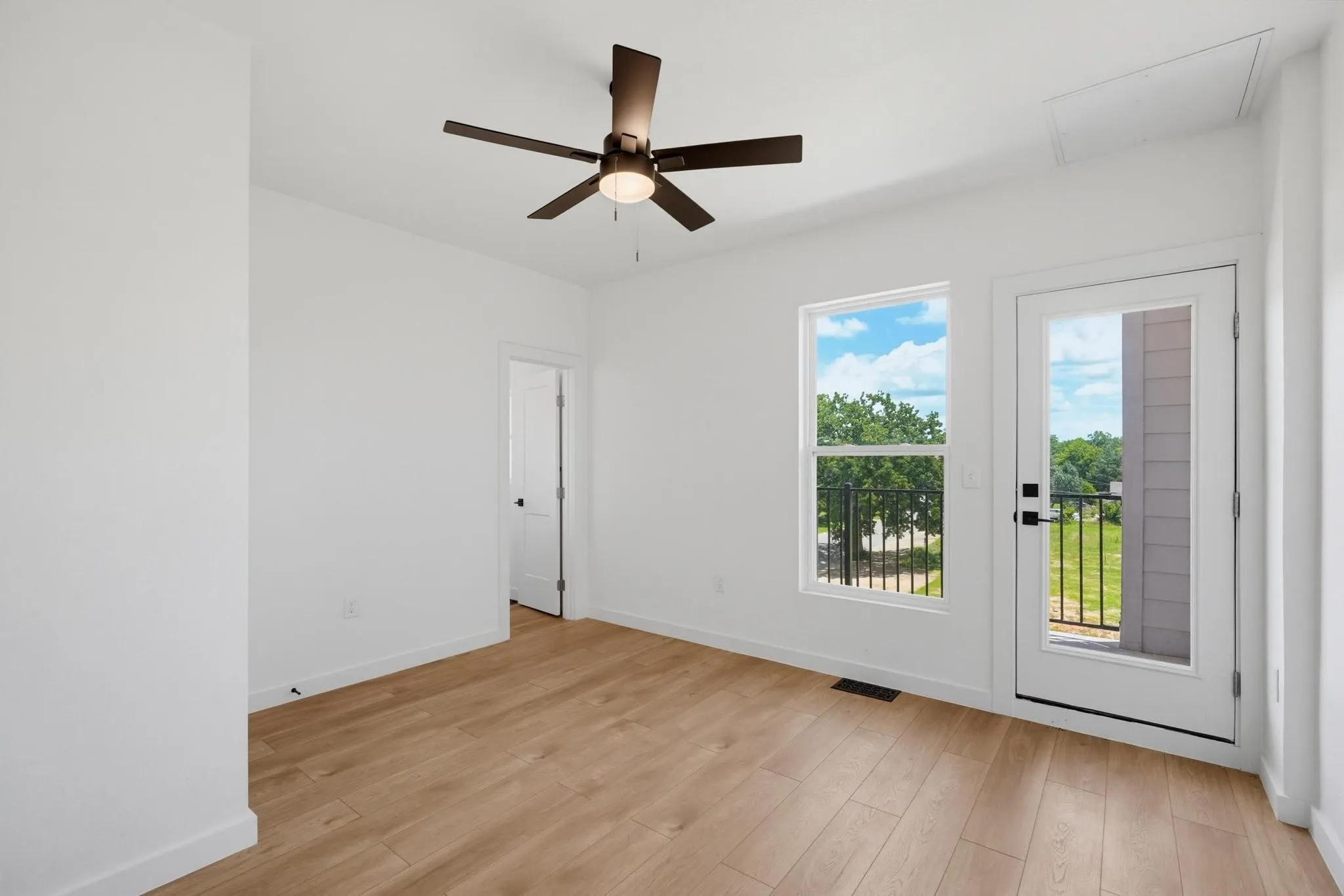 Spacious room featuring wood-finish flooring, a contemporary ceiling fan, ample natural light from the window, and direct exterior access through a glass-paneled door