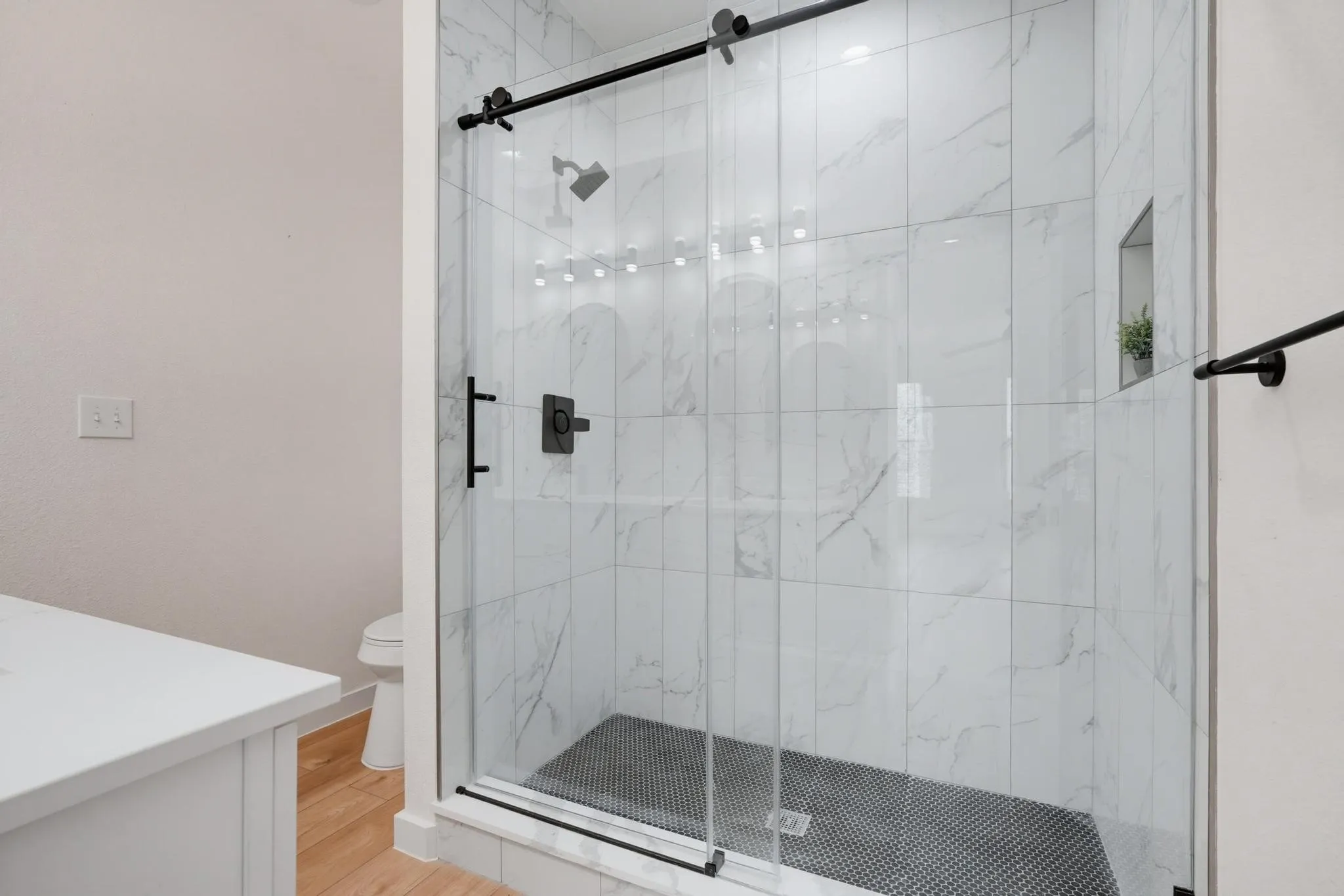 Modern shower enclosure featuring a glass sliding door with black hardware, white veined tile walls, and a black mosaic tile floor
