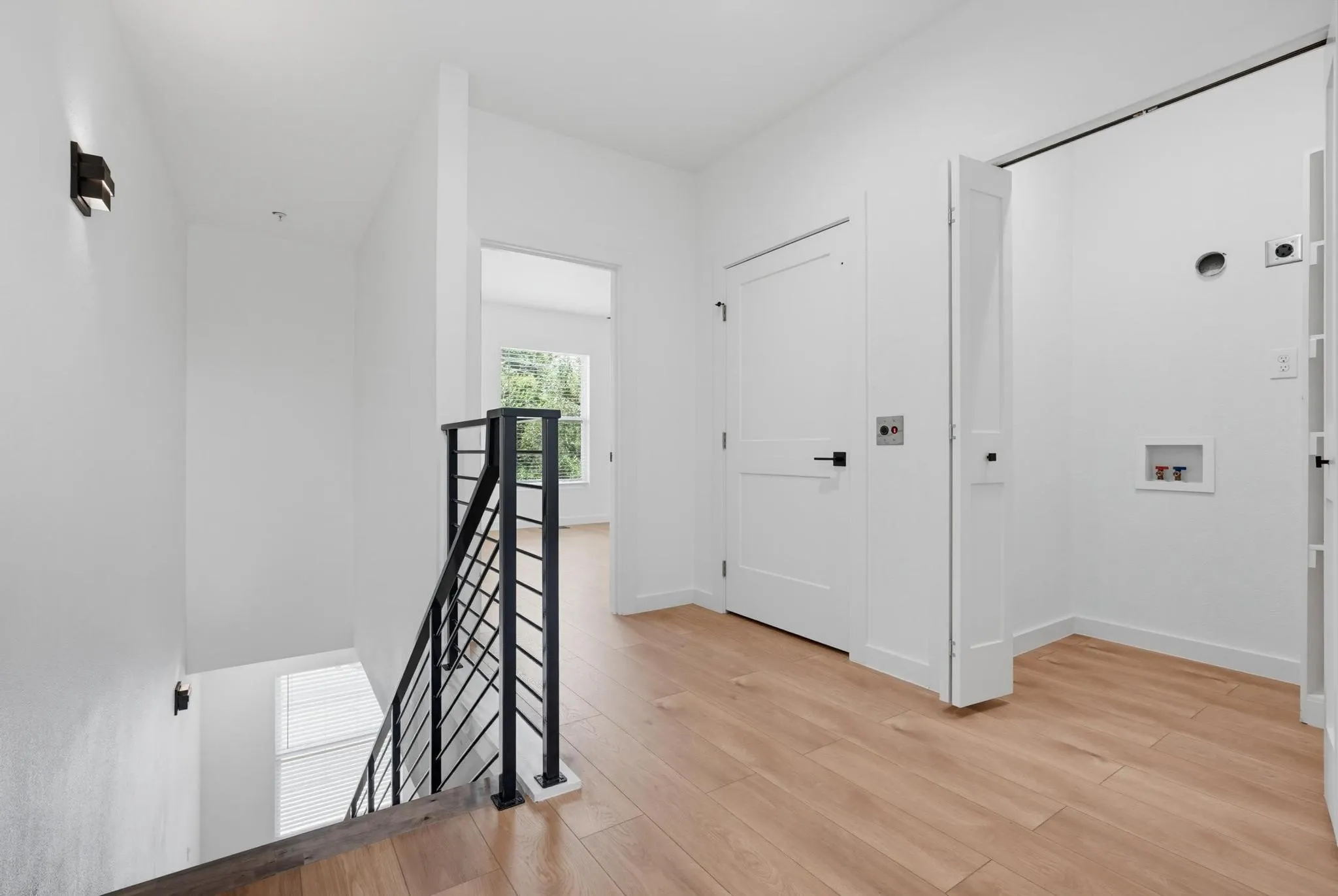 Contemporary interior landing featuring wood-finish flooring, a modern black metal stair railing, and crisp white walls