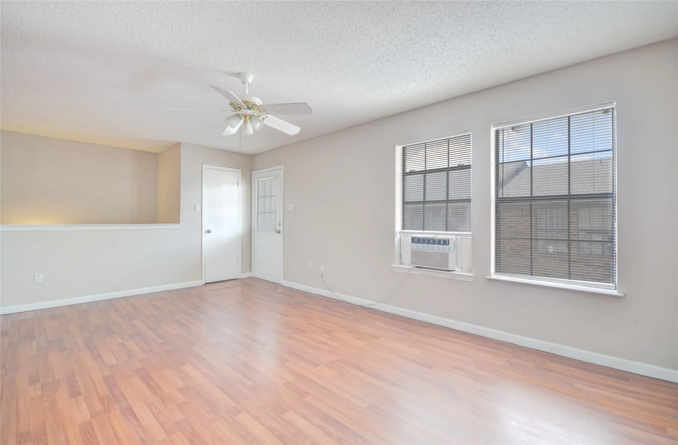 Spacious interior featuring luxury plank flooring, two large windows with blinds, a ceiling fan, and a half-wall architectural detail