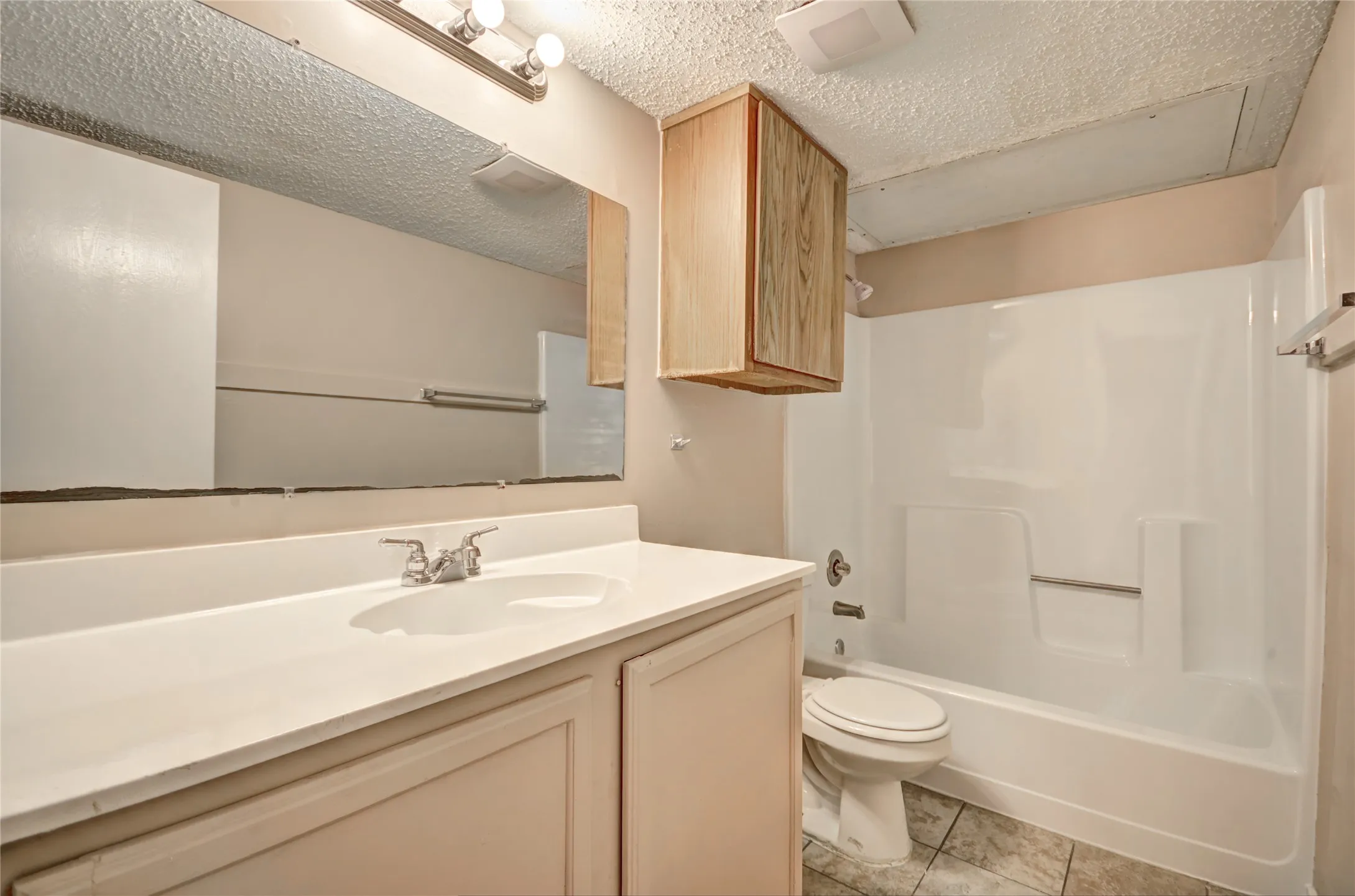 Bathroom featuring a vanity with an integrated sink, a large wall-mounted mirror, a separate wood-finish wall cabinet, seating area, and a combined shower-tub unit