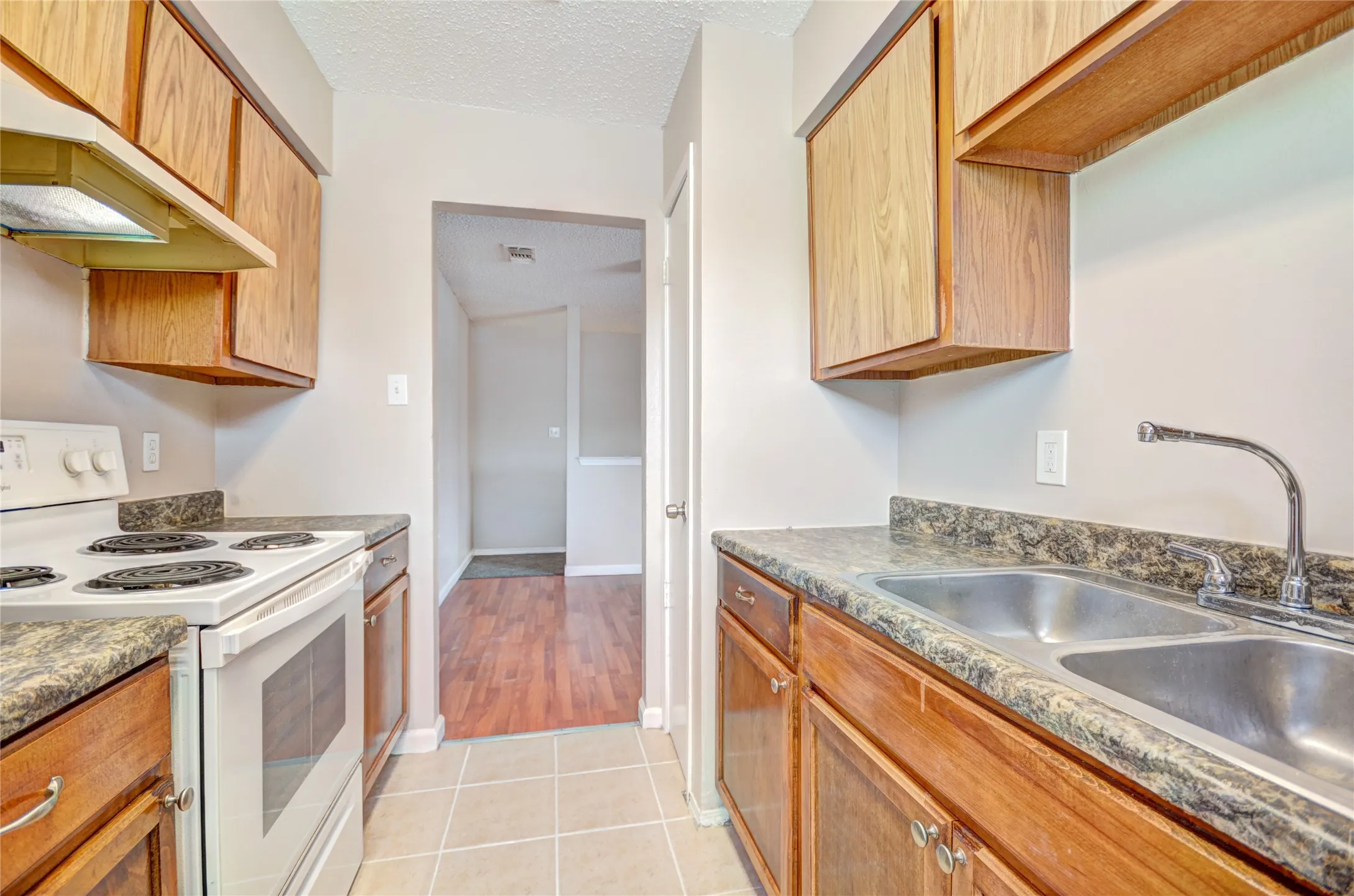 Galley kitchen featuring wood-finish cabinetry, upgraded countertops, and white appliances