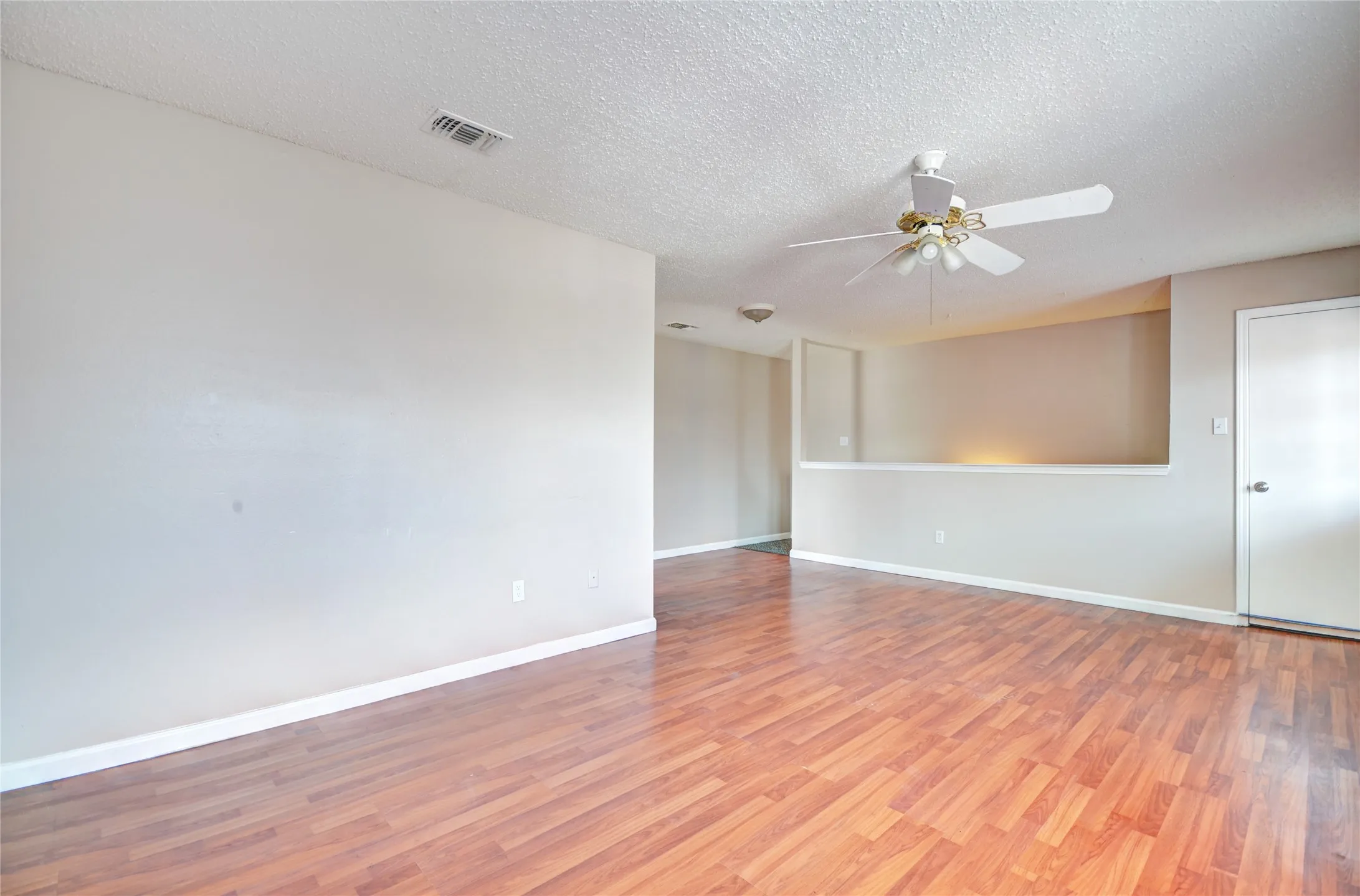 Spacious interior living area featuring luxury plank flooring, light neutral wall tones, and a ceiling fan with integrated lighting