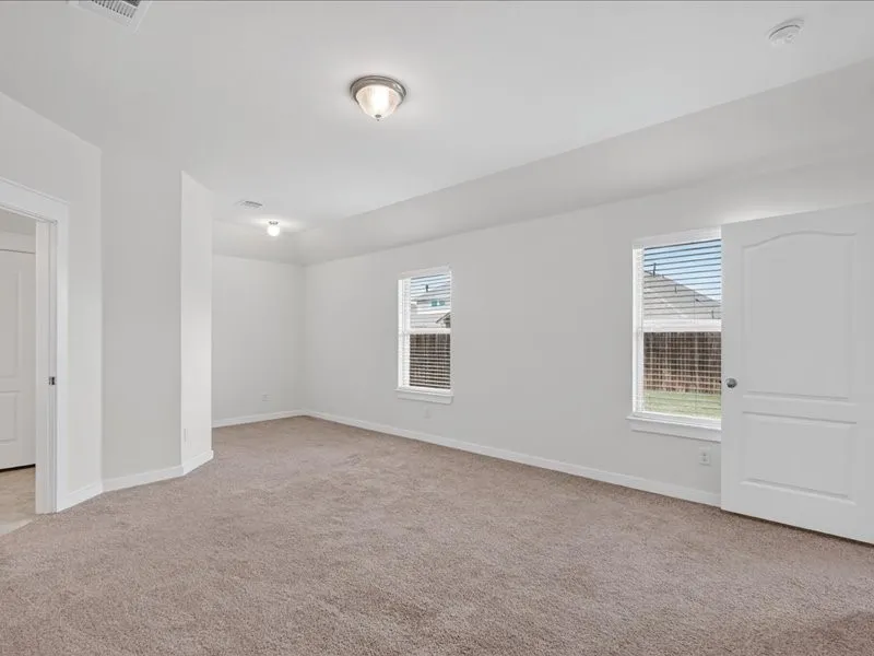 Spacious room featuring neutral carpeting, white walls, two windows with blinds, and a white paneled door