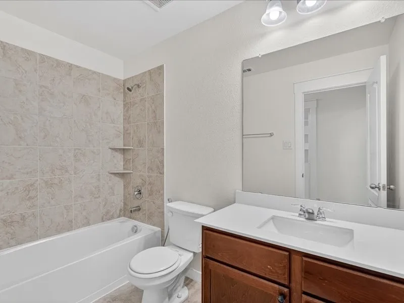 Bathroom featuring a white bathtub with light-toned tiled surround, integrated shelving, and a toilet