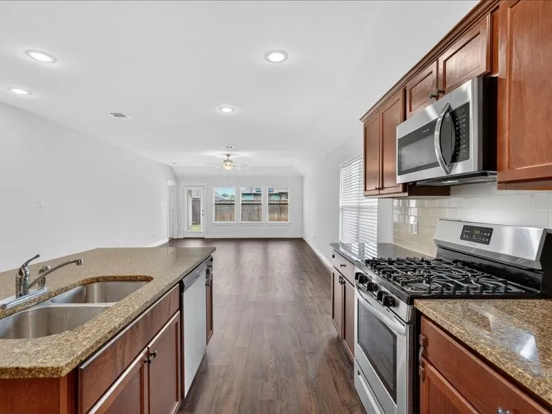 Kitchen featuring granite countertops, wood cabinetry, stainless steel appliances, and a tile backsplash