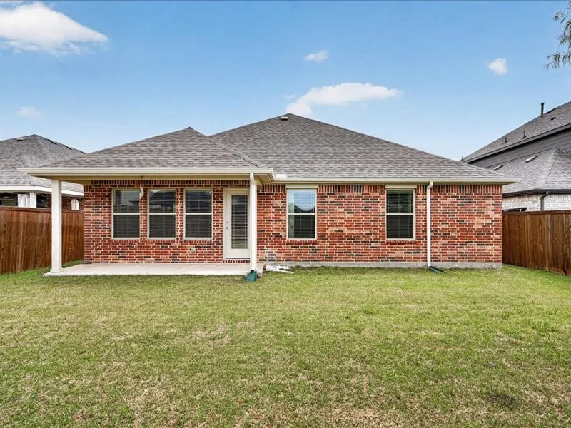 Rear exterior featuring a brick facade, covered patio, multiple windows, a glass-paneled door, and a grass lawn