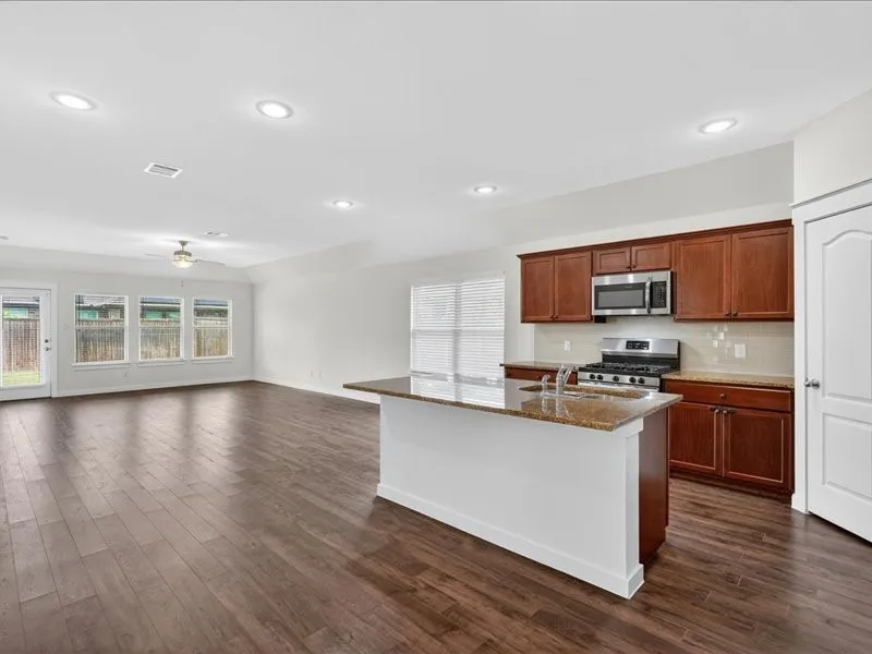 Open-concept kitchen and living area featuring wood-finish flooring, recessed lighting, and a kitchen island with stone countertop