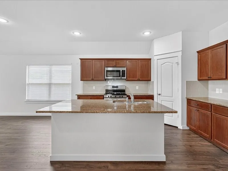 Kitchen featuring a large island with a double basin sink, stainless steel appliances, wood-finish flooring, recessed lighting, and a window with blinds