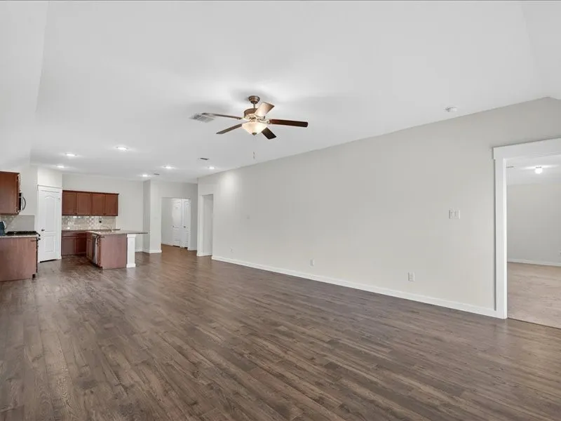 Spacious living area featuring wood-finish flooring, light-toned walls, and a ceiling fan