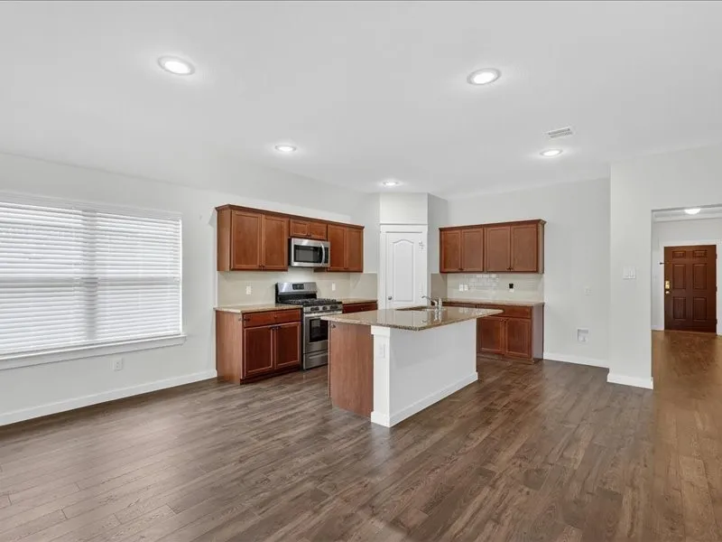 Open-concept kitchen and living area featuring dark wood-finish flooring, recessed lighting, a kitchen island with a built-in sink, stainless steel appliances, and wood cabinetry