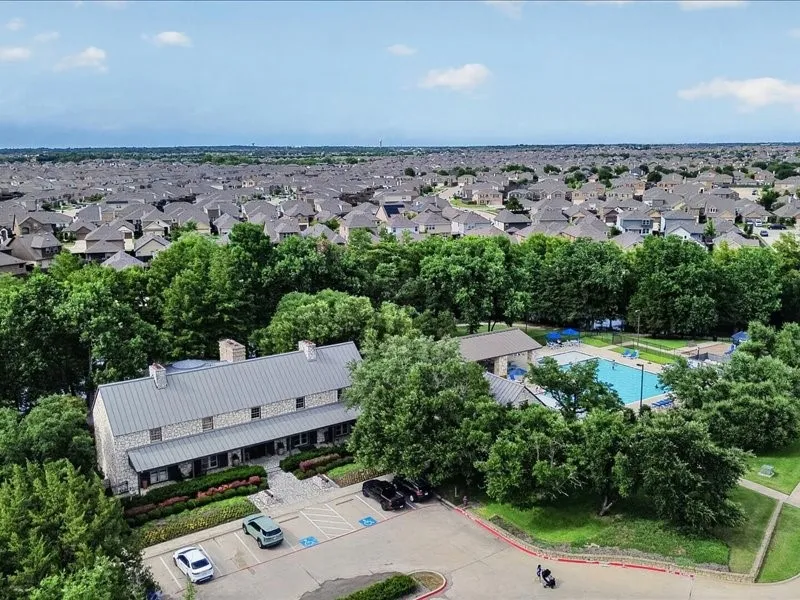 Stone-clad amenity building featuring a metal roof, surrounded by mature trees, a swimming pool, and dedicated parking