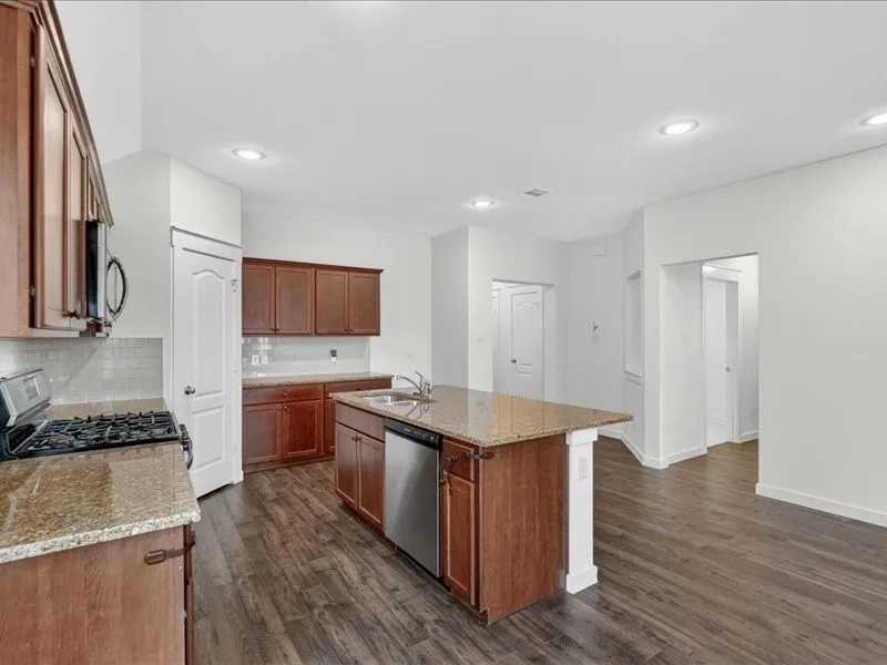 Kitchen featuring an island with a stainless-steel sink, granite countertops, wood-finish flooring, recessed lighting, and white subway tile backsplash