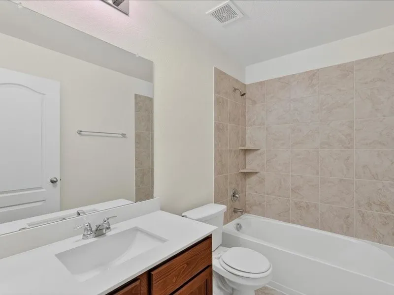 Bathroom featuring a single vanity with an integrated sink and chrome faucet, a large frameless mirror, a shower-over-tub with tiled surround, and built-in shower shelves