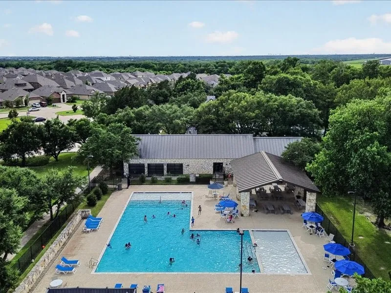 Outdoor swimming pool area featuring a stone-clad building with a metal roof, an adjacent covered pavilion, and surrounding paved decking