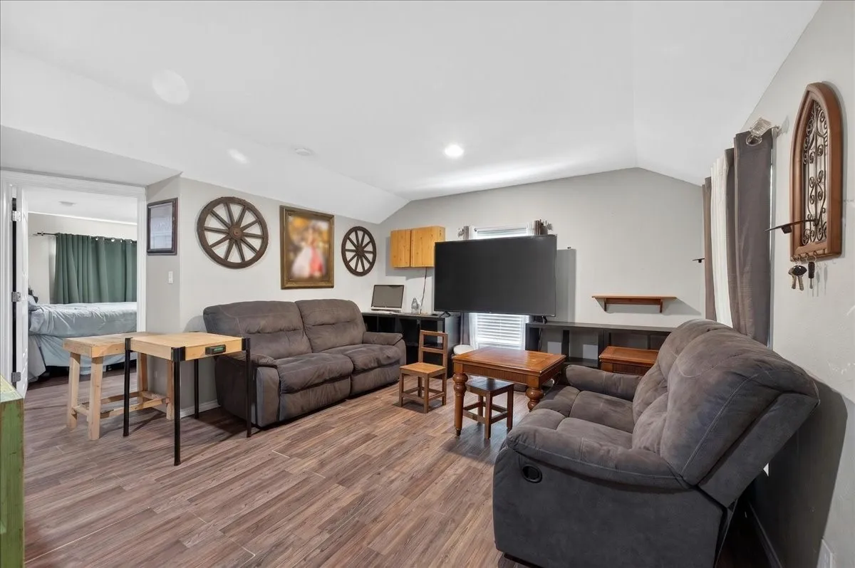 Spacious room featuring wood-finish flooring, light grey walls, and a vaulted ceiling