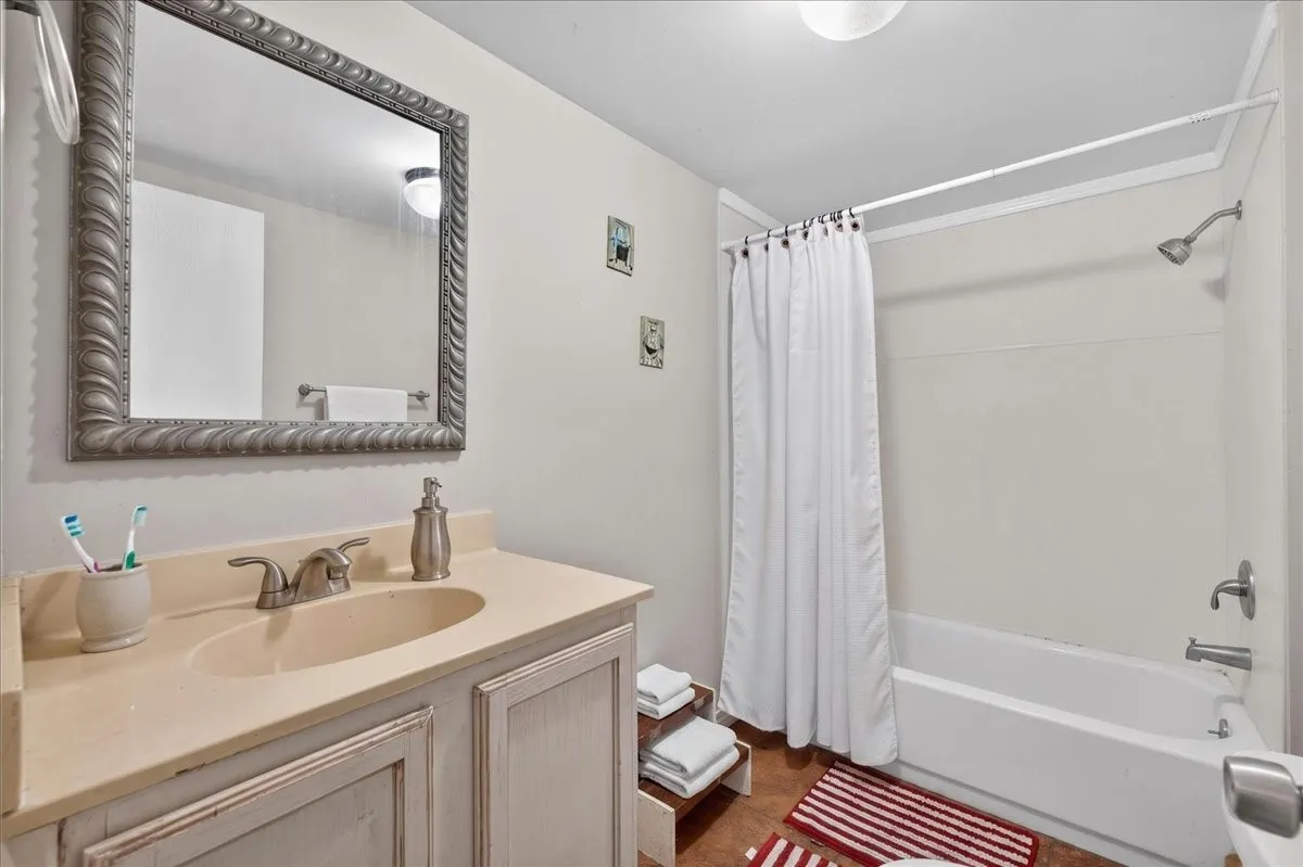 Bathroom featuring a vanity with an integrated sink and light-toned countertop, a decorative framed mirror, and a full-size bathtub with an overhead shower fixture