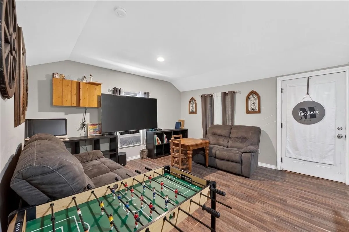Spacious room featuring vaulted ceilings, wood-finish flooring, recessed lighting, and a white paneled door
