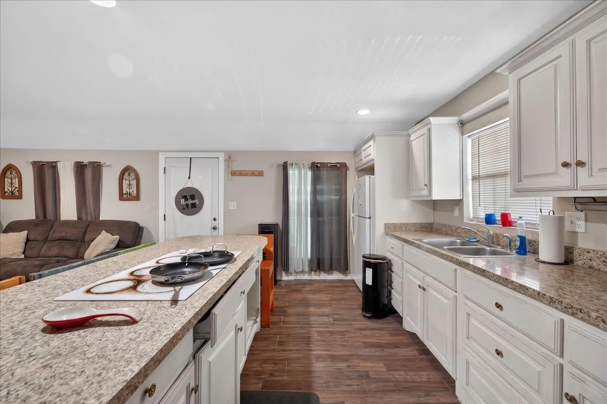 Open-concept kitchen featuring white cabinetry, granite-finish countertops, and wood-finish flooring