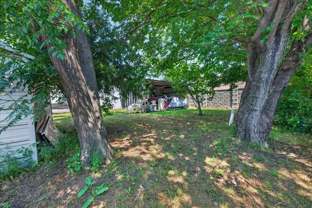 Expansive outdoor space featuring mature trees, a stone-faced retaining wall, and a white siding structure