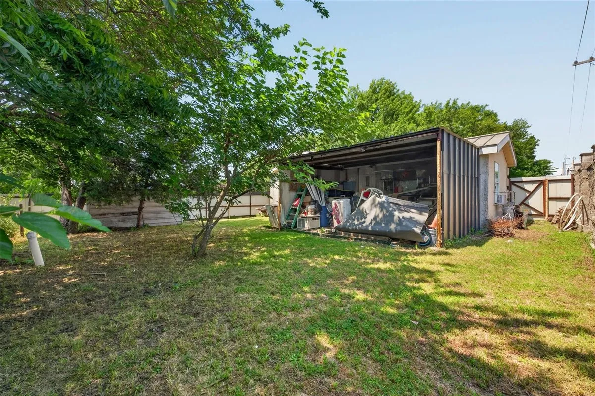 Expansive outdoor space featuring a covered storage structure, detached accessory building, and mature trees