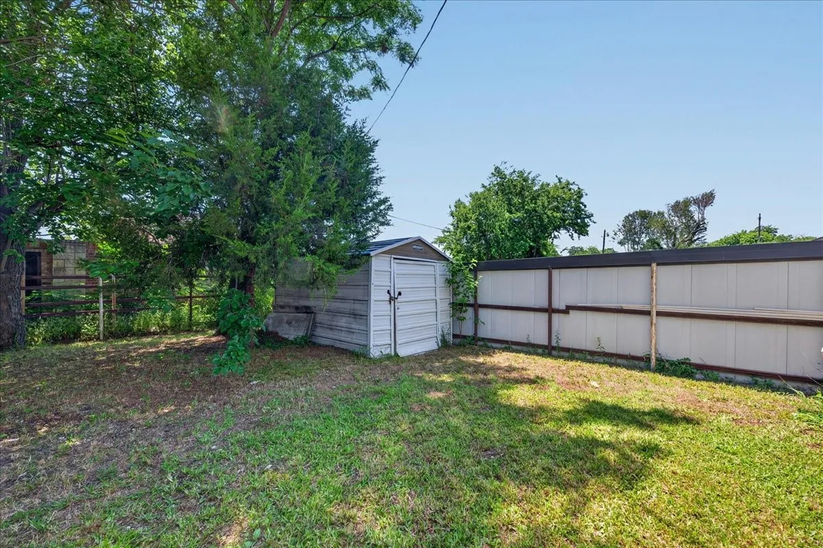 Expansive backyard featuring a storage shed, mature trees, and privacy fencing
