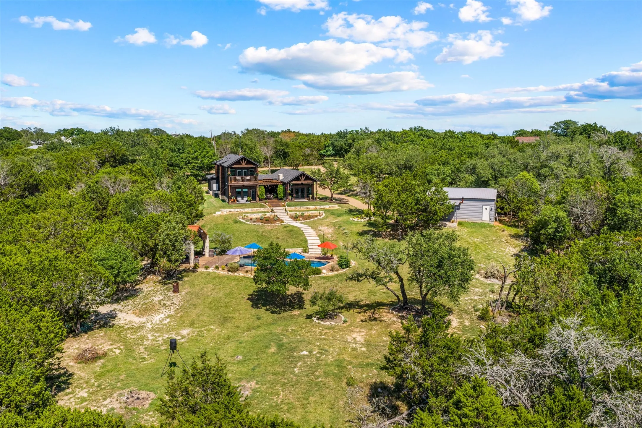 Expansive property featuring a multi-level residence with dark exterior siding, an outdoor swimming pool, and a detached auxiliary building