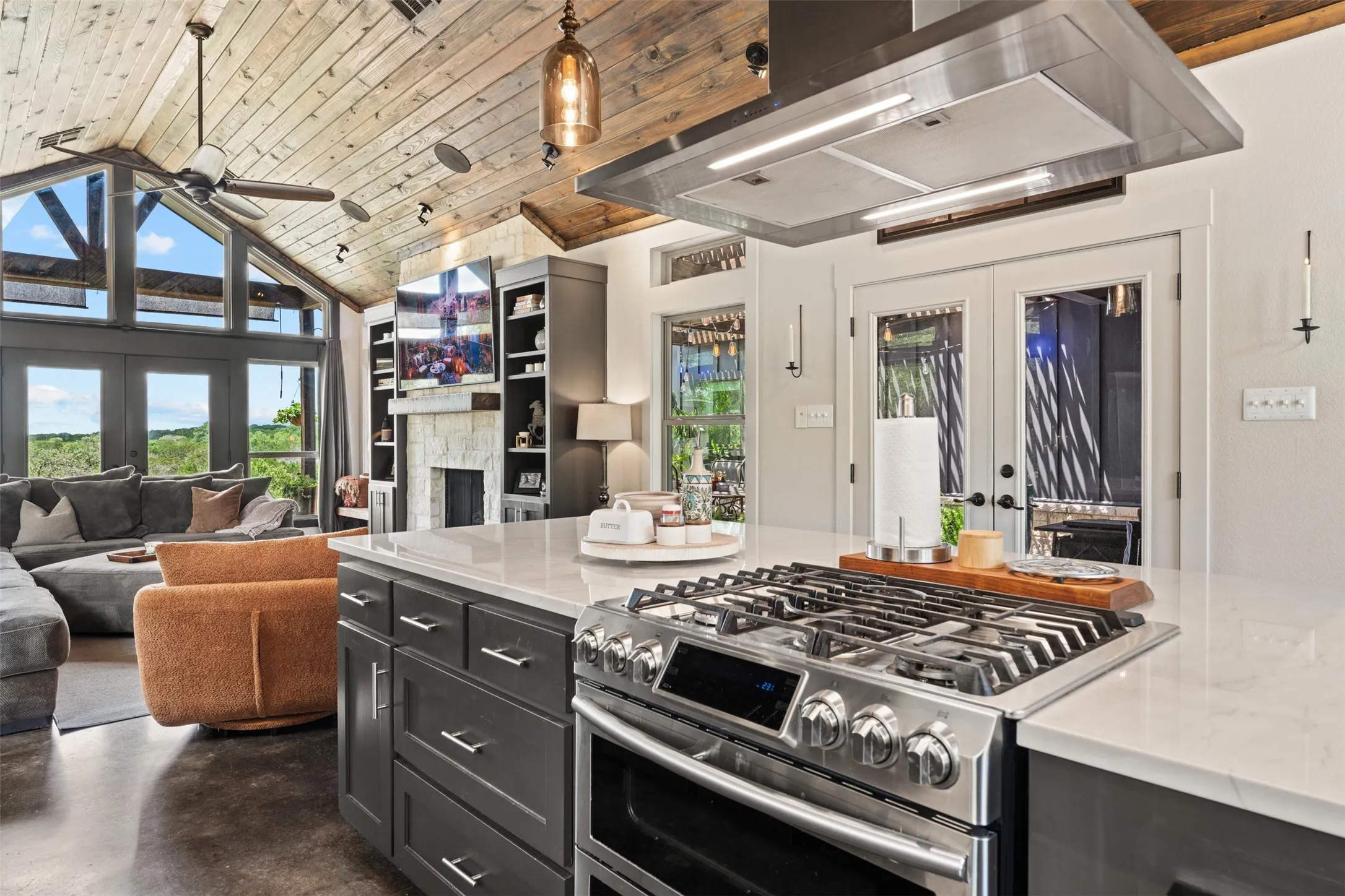 Gourmet kitchen island with a gas range and stainless steel hood, featuring white countertops and dark cabinetry