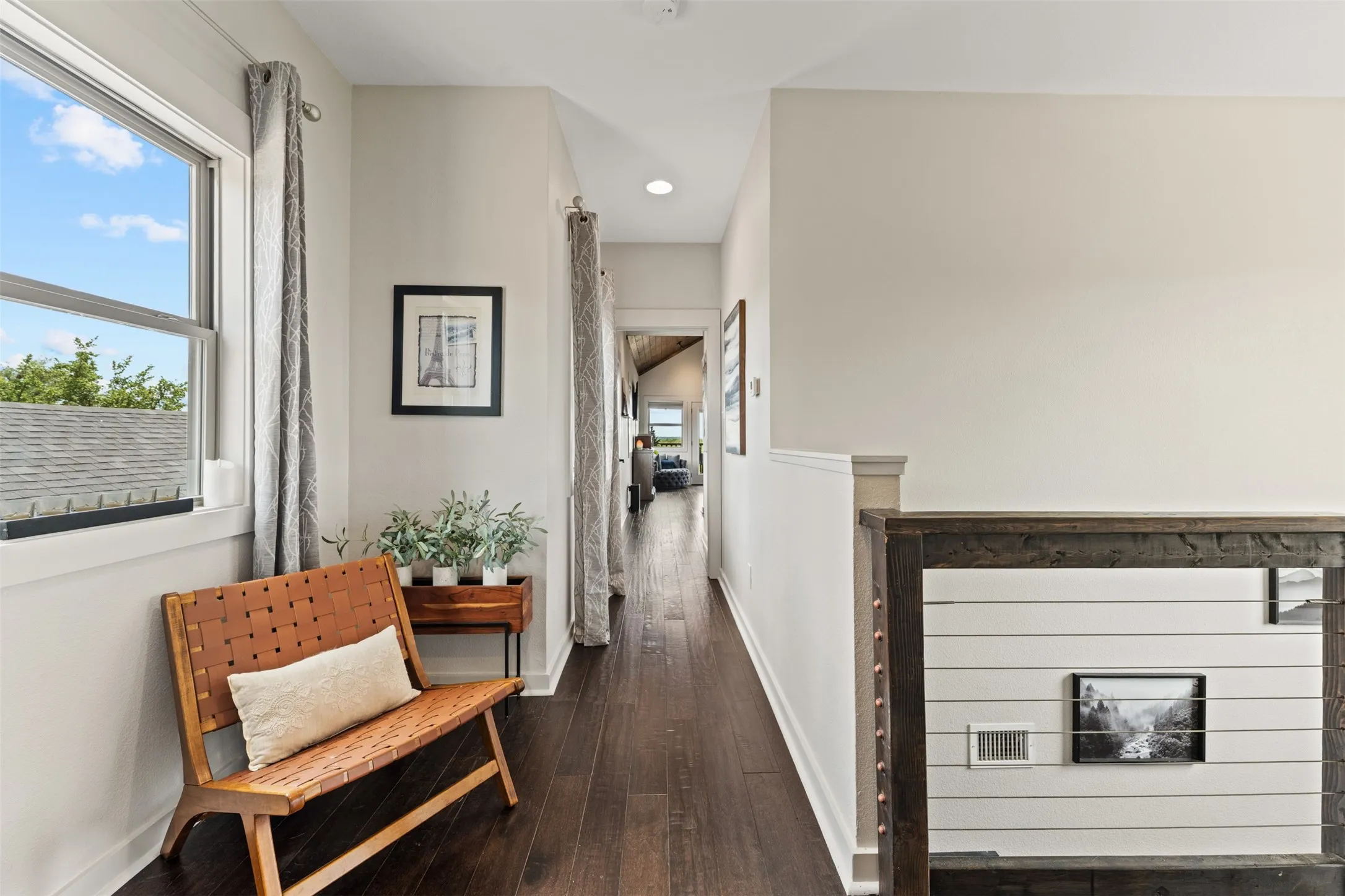 Upper-level hallway to primary bedroom featuring dark wood-finish flooring, a contemporary window with natural light, recessed ceiling lighting, a white painted railing with cable infill, and wainscoting
