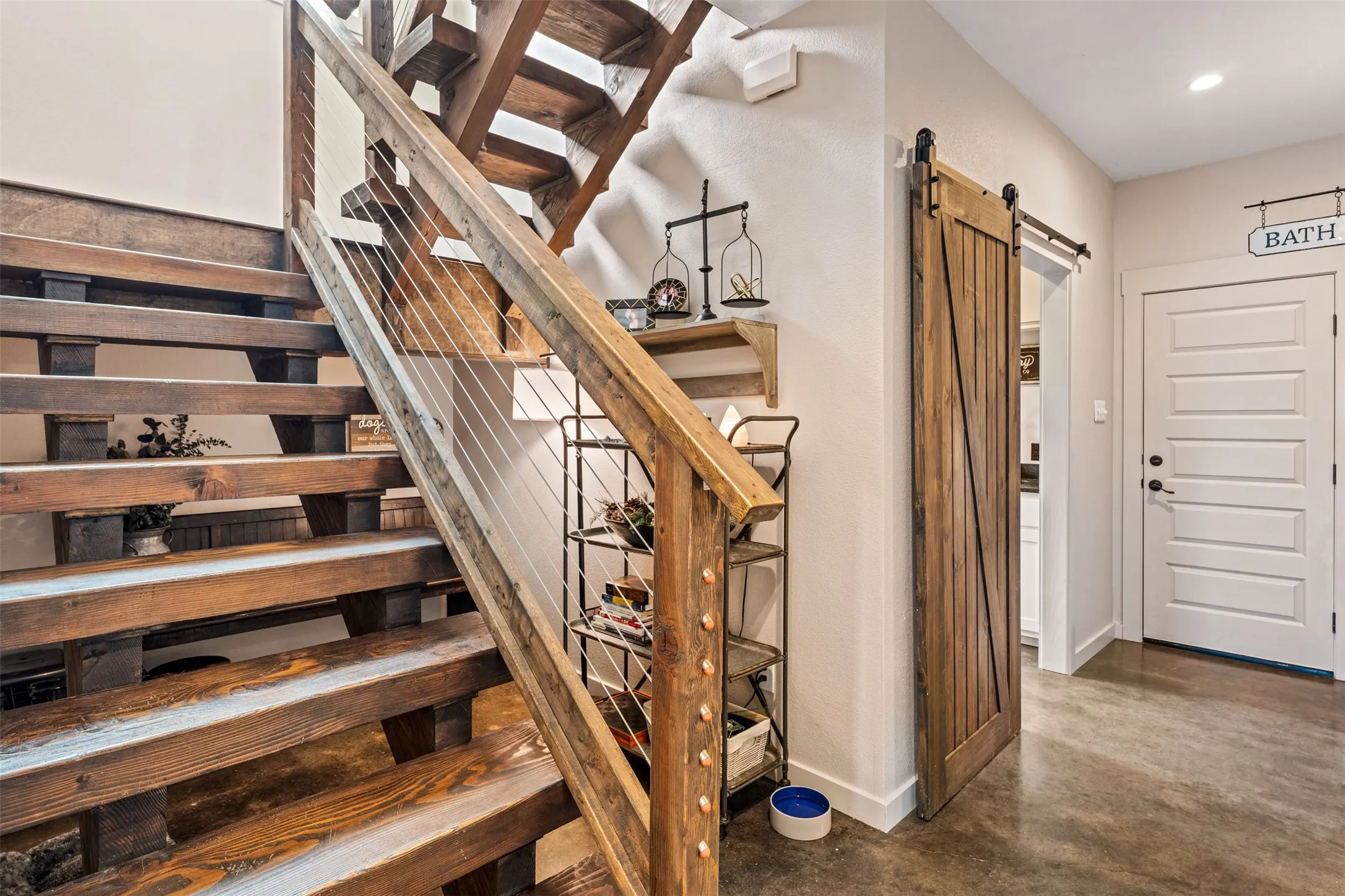 Wood-finish staircase with cable railing, concrete flooring, wood-finish barn door, and a five-panel interior door