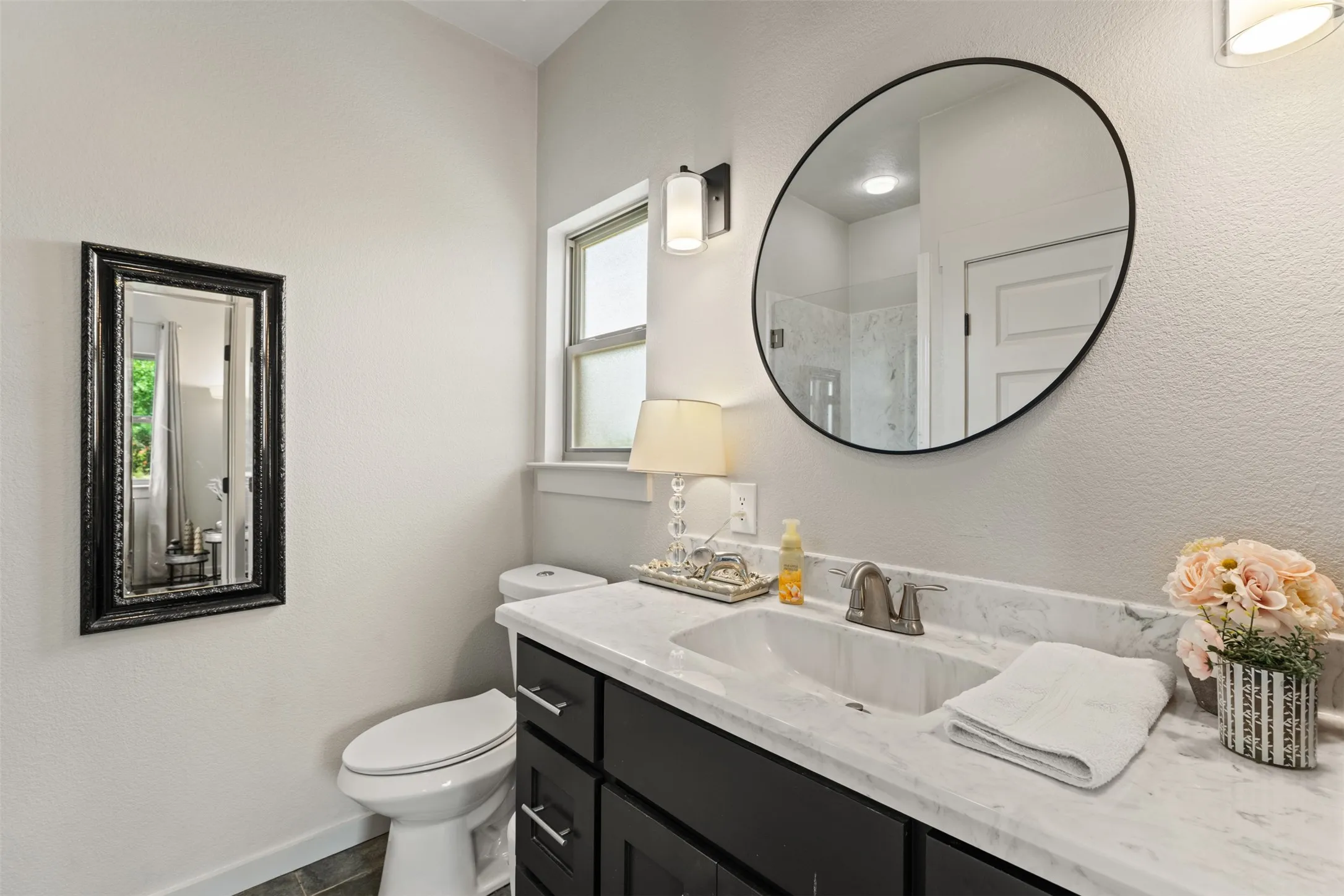 Bathroom featuring a dark wood-finish vanity with a white countertop and integrated sink, a large circular mirror with a black frame, and wall-mounted light fixtures