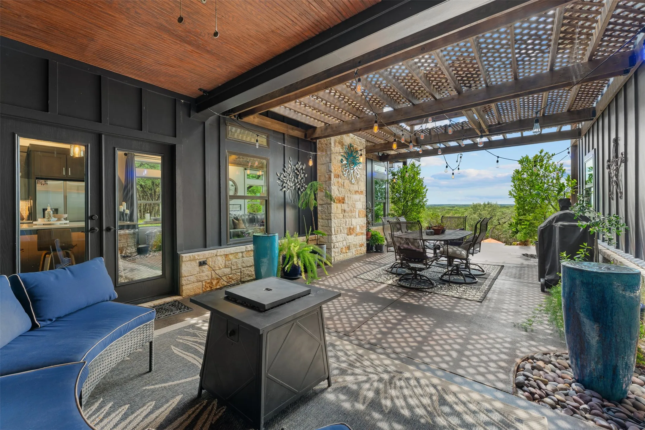 Covered outdoor patio featuring a wood-finish ceiling, stone veneer accents, and a slatted pergola