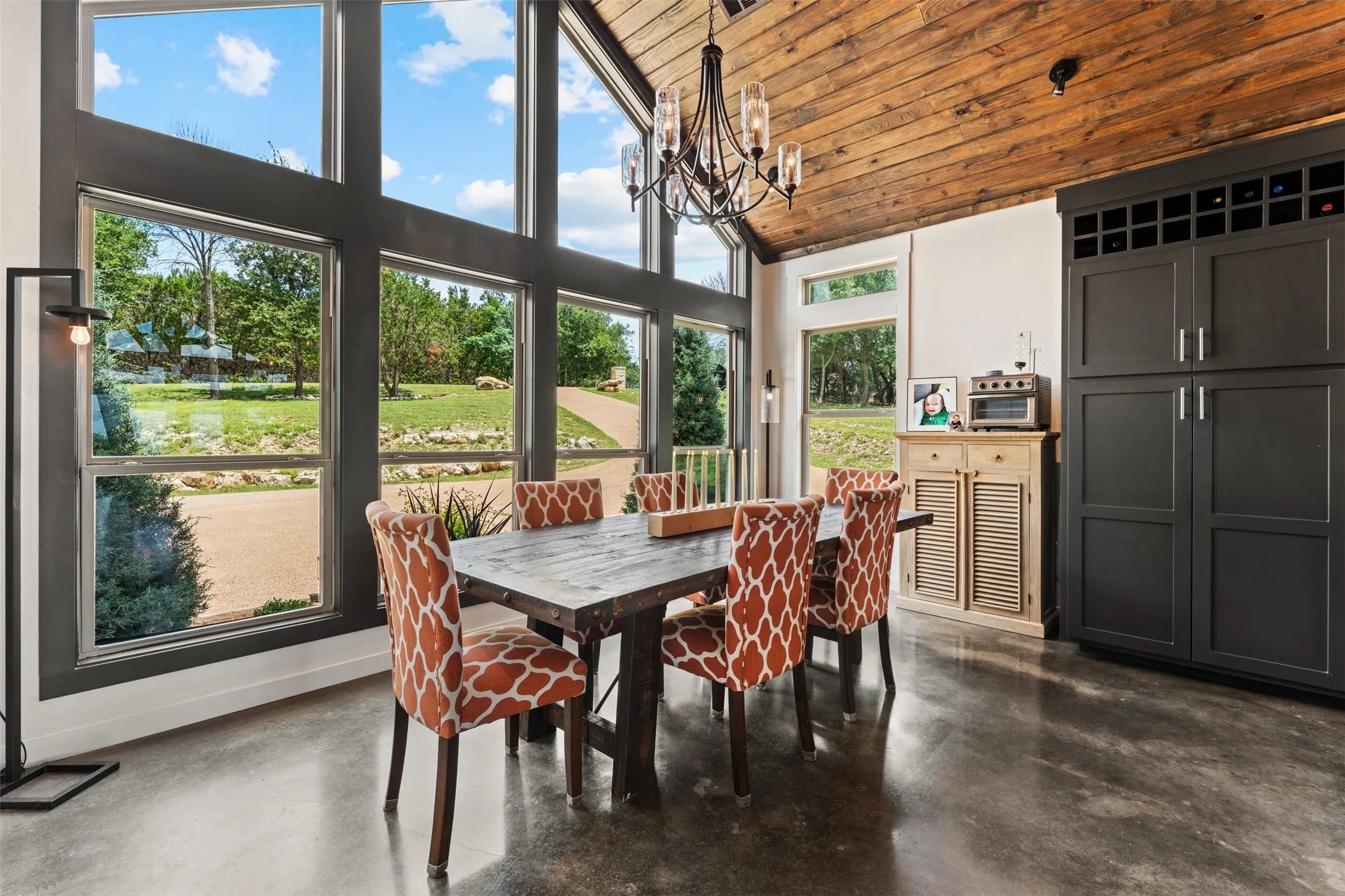 Vaulted wood-paneled ceiling with a chandelier, expansive windows, polished concrete flooring, and built-in cabinetry with a wine rack