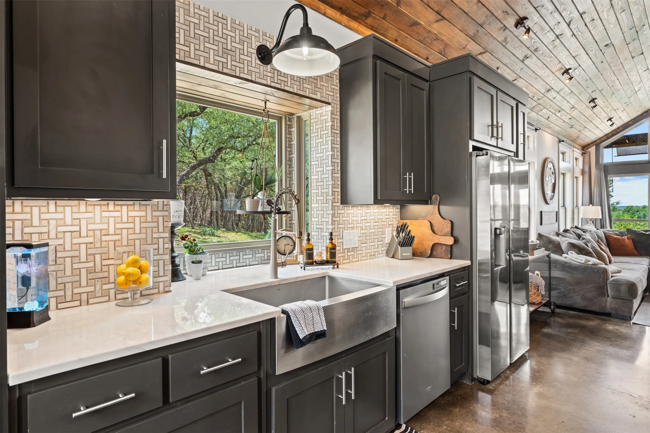 Modern kitchen featuring dark cabinetry, stainless steel appliances, a farmhouse sink, light countertops, and a patterned tile backsplash
