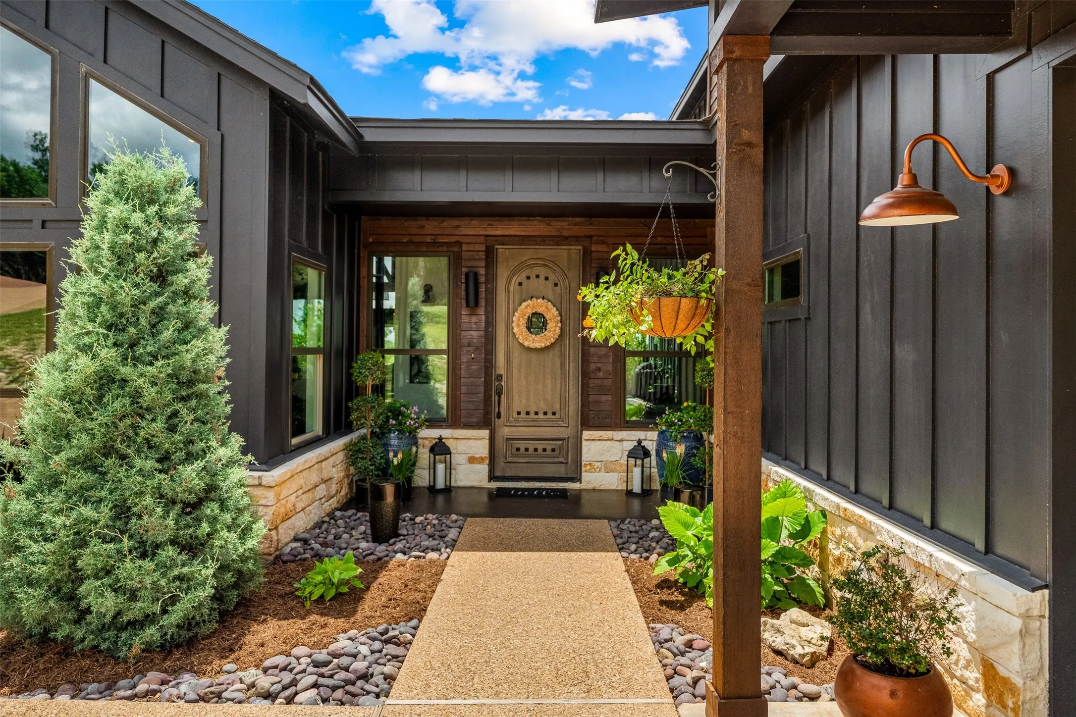 Inviting front entry featuring a stained wood door, board and batten siding, stone accents, a concrete walkway, and an arched outdoor light fixture