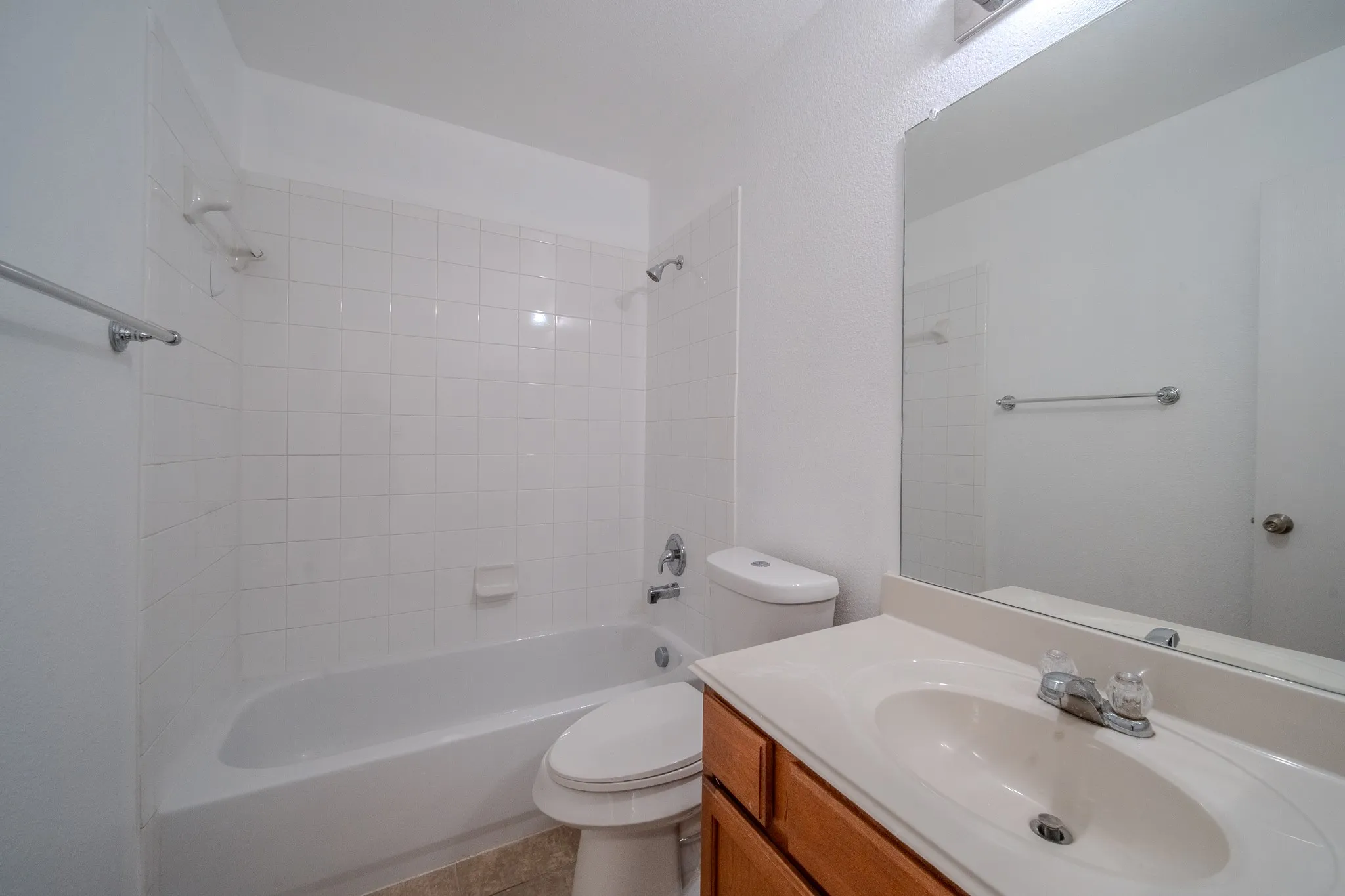 Bathroom featuring a white subway tile surround bathtub with shower, a vanity with a light-colored countertop and integrated sink, a large wall-mounted mirror, a toilet, and light-toned flooring