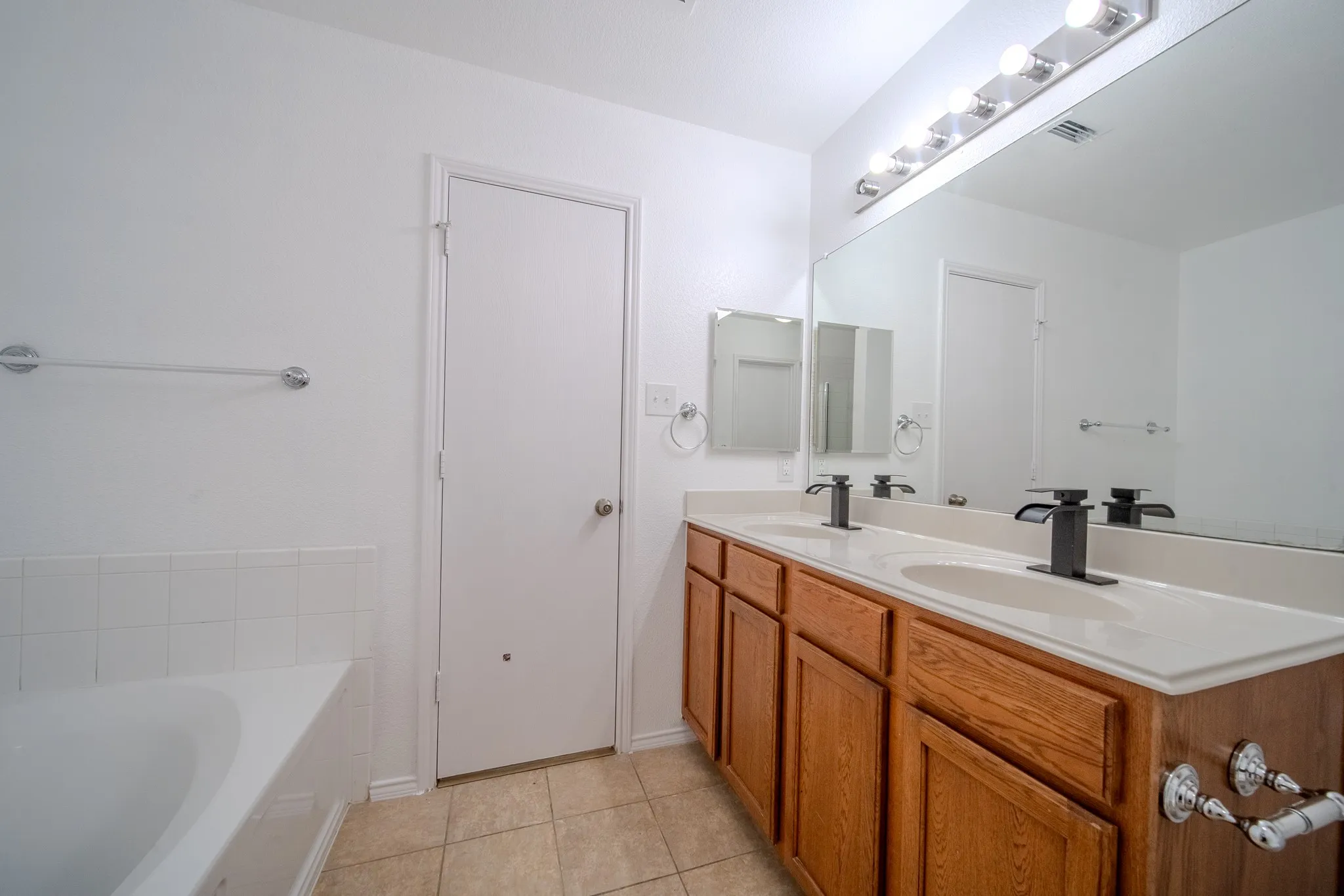 Double vanity with wood cabinetry, light-toned countertop, and matte black faucets