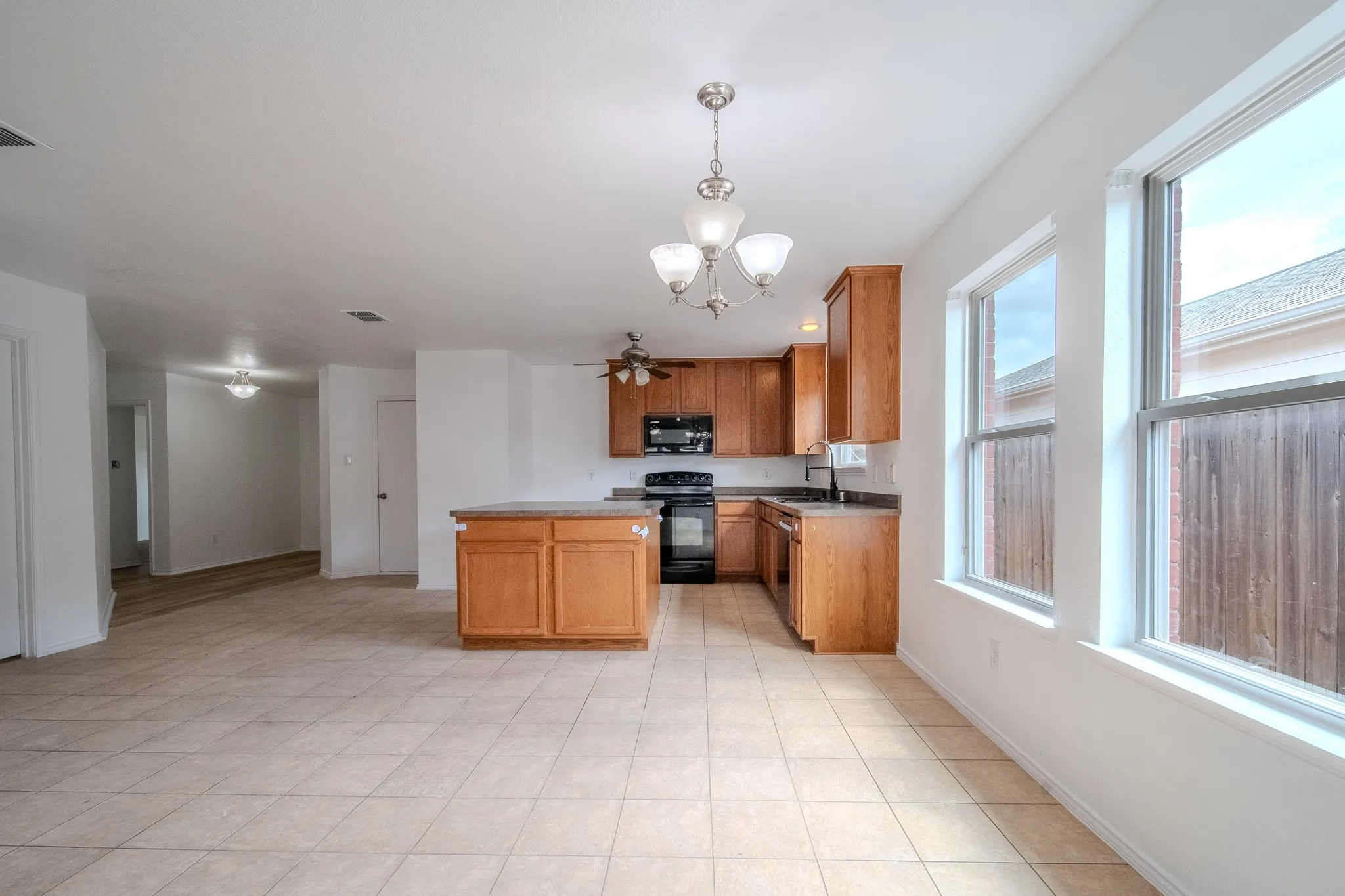 Open-concept kitchen and living area featuring tile flooring, light wood cabinetry, a central island, and multiple windows