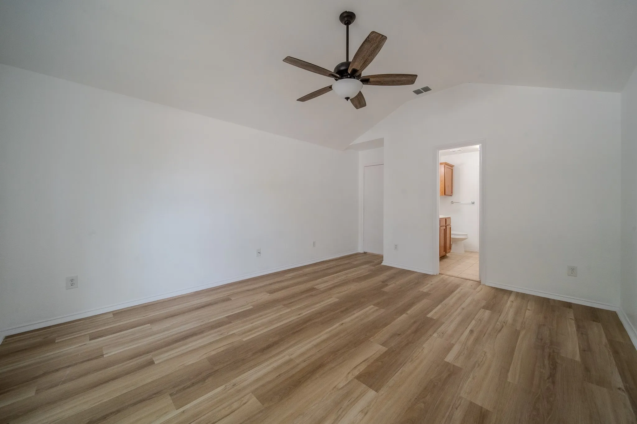 Vaulted ceiling bedroom with wood-finish flooring, ceiling fan, and direct access to a private bathroom featuring a vanity with wood cabinetry