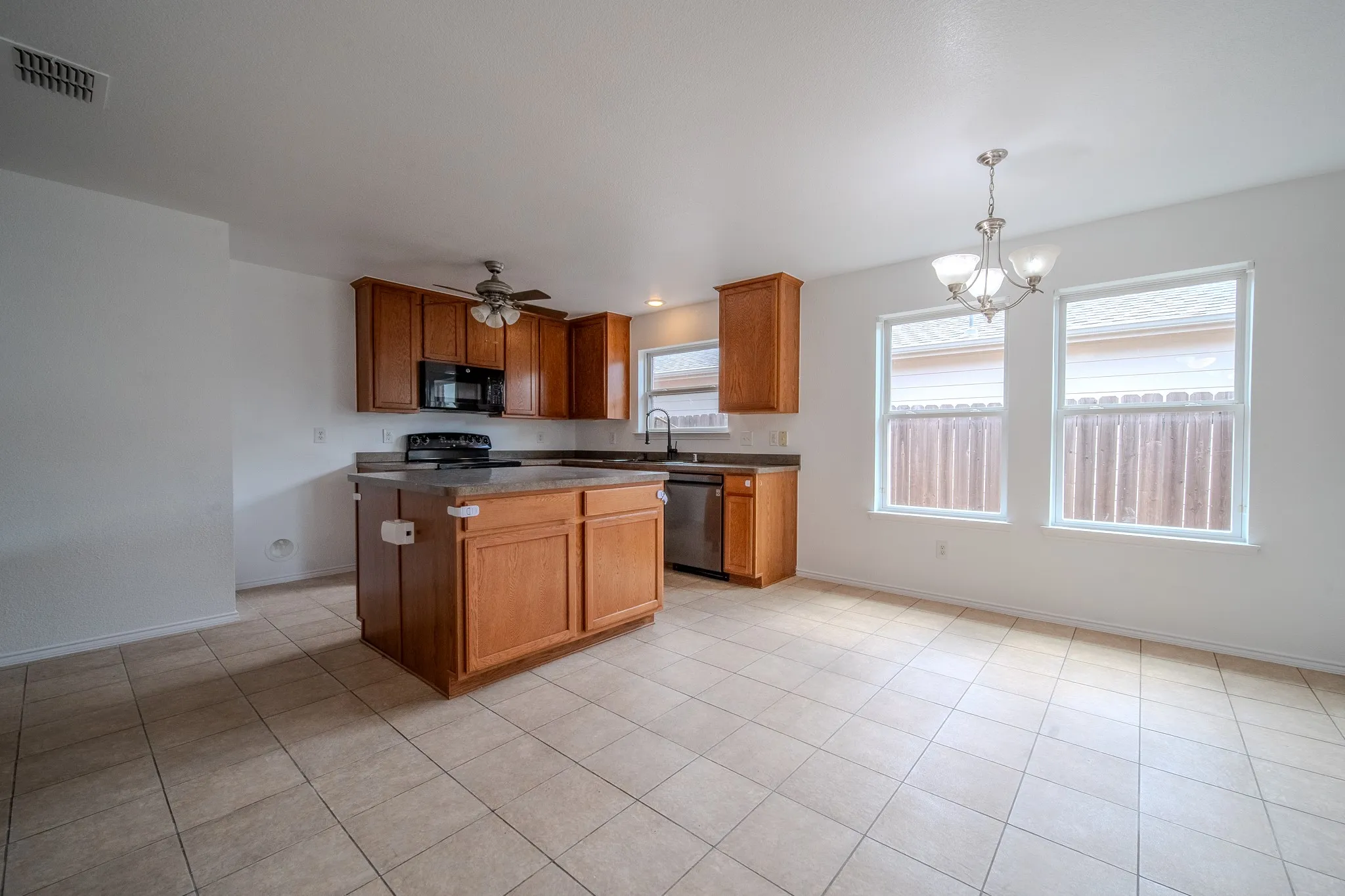 Open-concept kitchen and dining area featuring a central island, wood-finish cabinetry, black appliances, and tile flooring