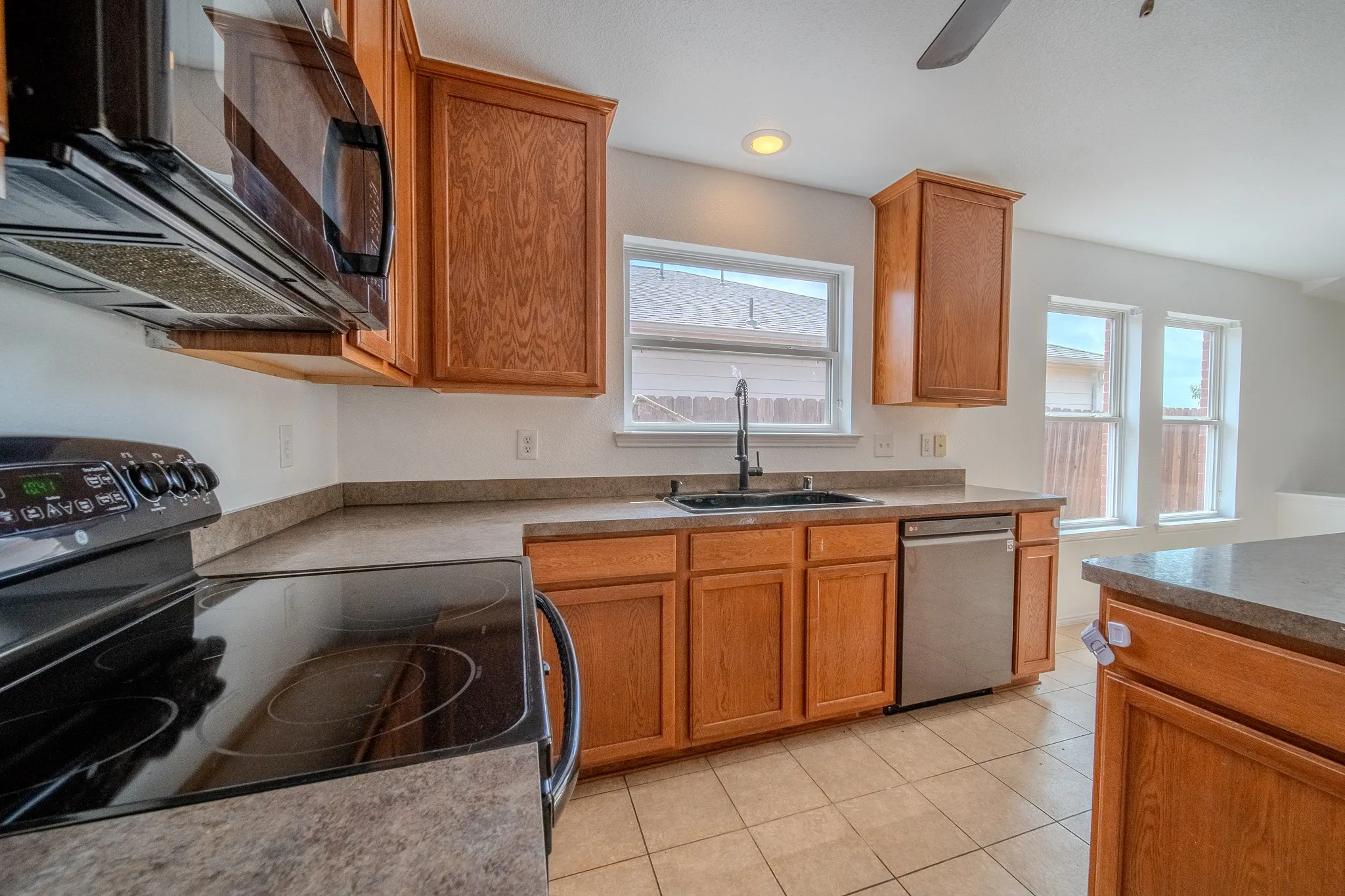 Kitchen featuring wood-finish cabinetry, a black electric range with an over-the-range microwave, a stainless steel dishwasher, and a black faucet with a single basin sink